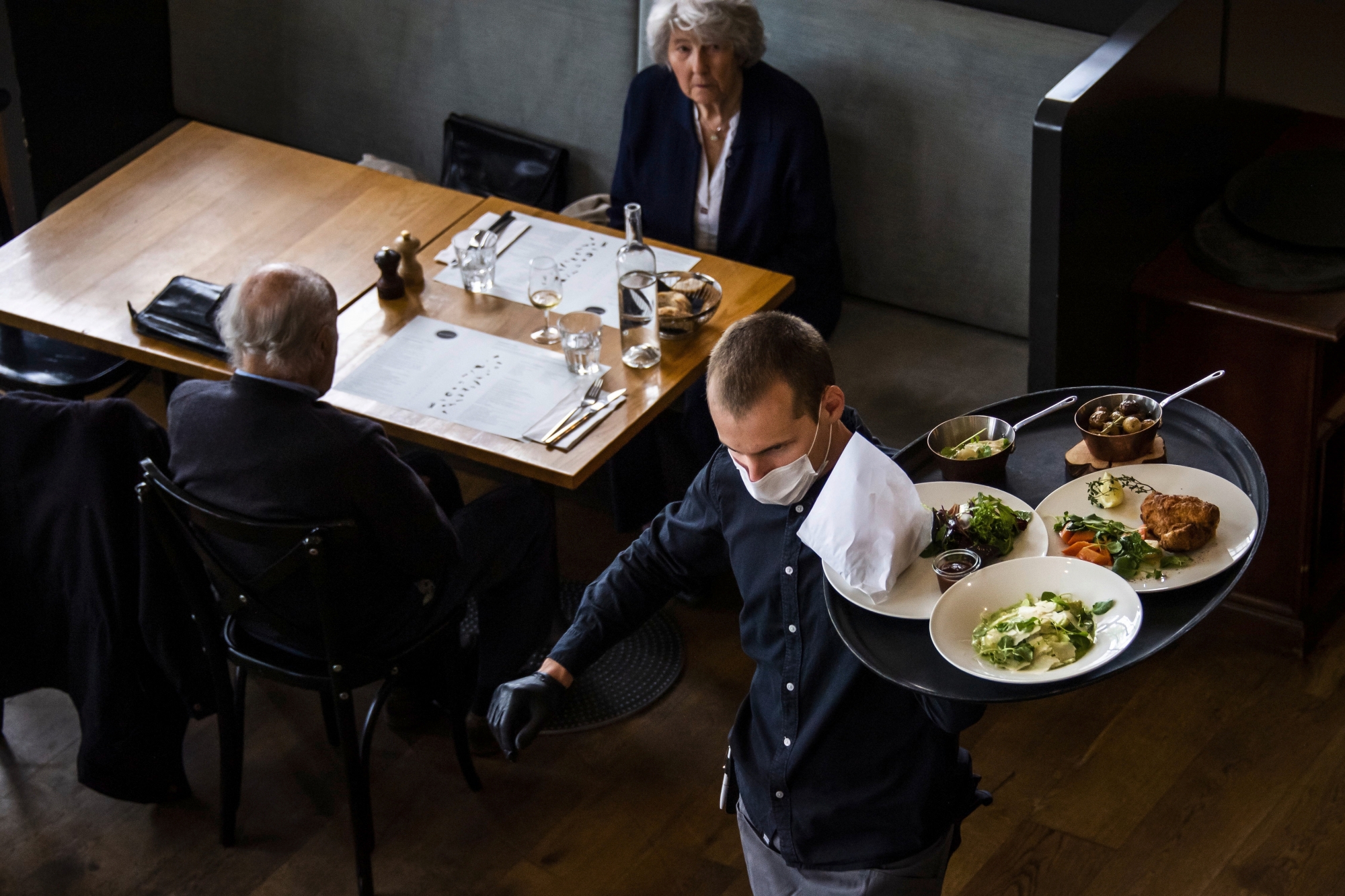 A waiter of "La Brasserie de Montbenon" restaurant brings dishes food to customers during the spread of the pandemic Coronavirus (COVID-19) disease in Lausanne, Switzerland, Monday, May 11, 2020. In Switzerland from today, the Swiss authorities lifted second part of the lockdown. (KEYSTONE/Jean-Christophe Bott) ArcInfo