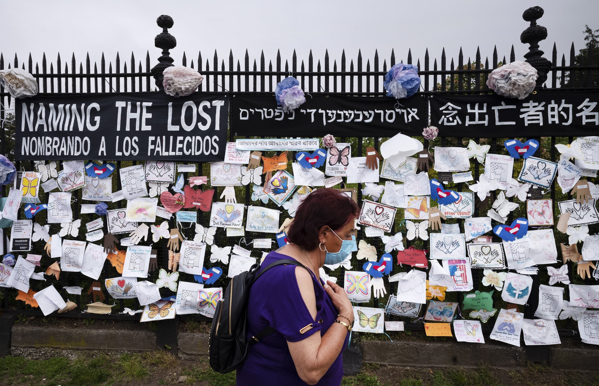 FILE - In this May 28, 2020, file photo, a woman passes a fence outside Brooklyn's Green-Wood Cemetery adorned with tributes to victims of COVID-19 in New York. The U.S. death toll from the coronavirus topped 200,000 Tuesday, Sept. 22, a figure unimaginable eight months ago when the scourge first reached the world&#x201a;Äôs richest nation with its sparkling laboratories, top-flight scientists and towering stockpiles of medicines and emergency supplies. (AP Photo/Mark Lennihan, File) ArcInfo
