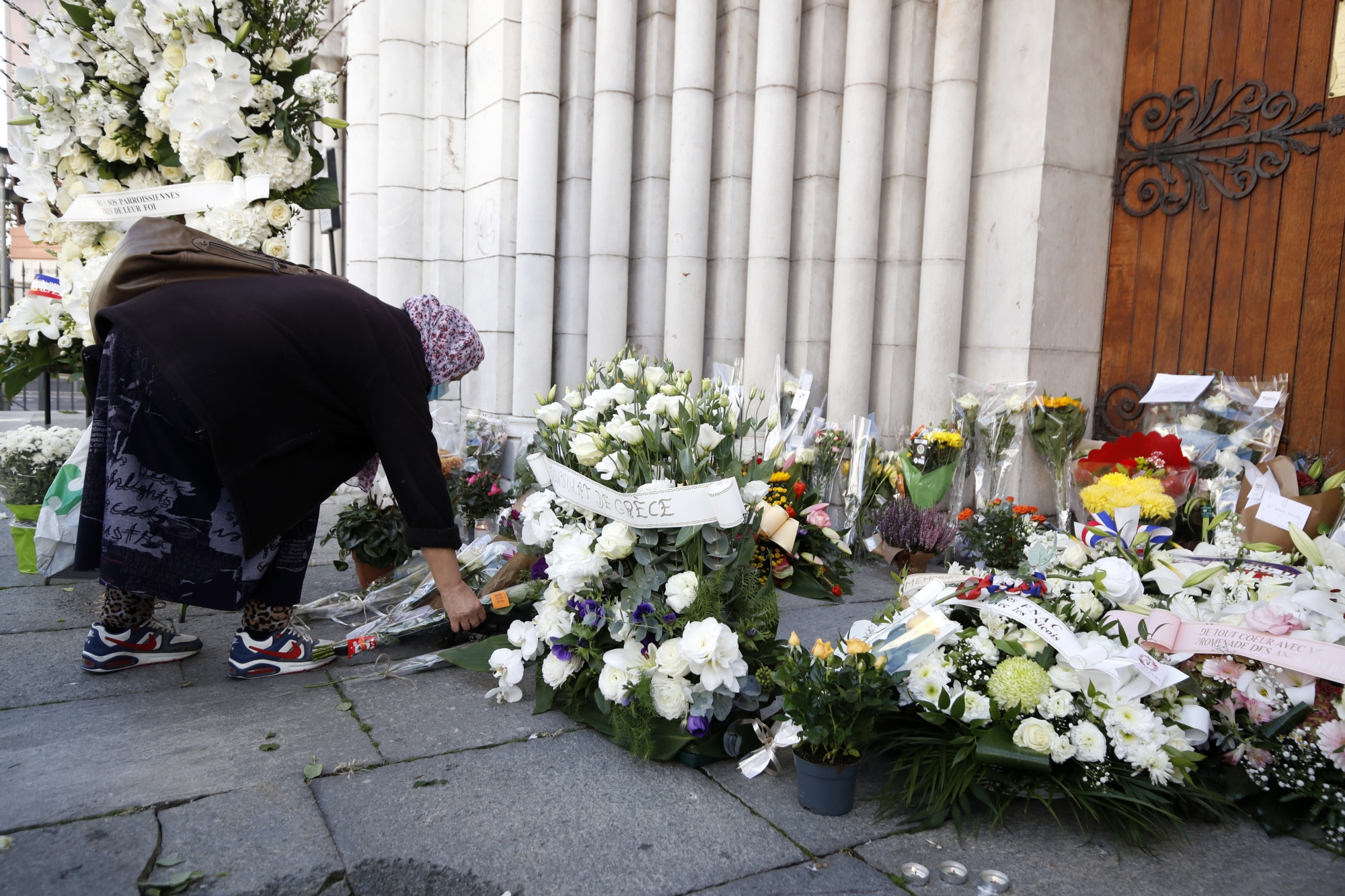 epa08785649 A woman lays flowers on a makeshift memorial to the victims of the knife attack at the entrance of the Notre Dame Basilica church in Nice, France, 30 October 2020. Three people have died in a terror attack. The attack comes less than a month after the beheading of a French middle school teacher in Paris on 16 October.  EPA/SEBASTIEN NOGIER ArcInfo