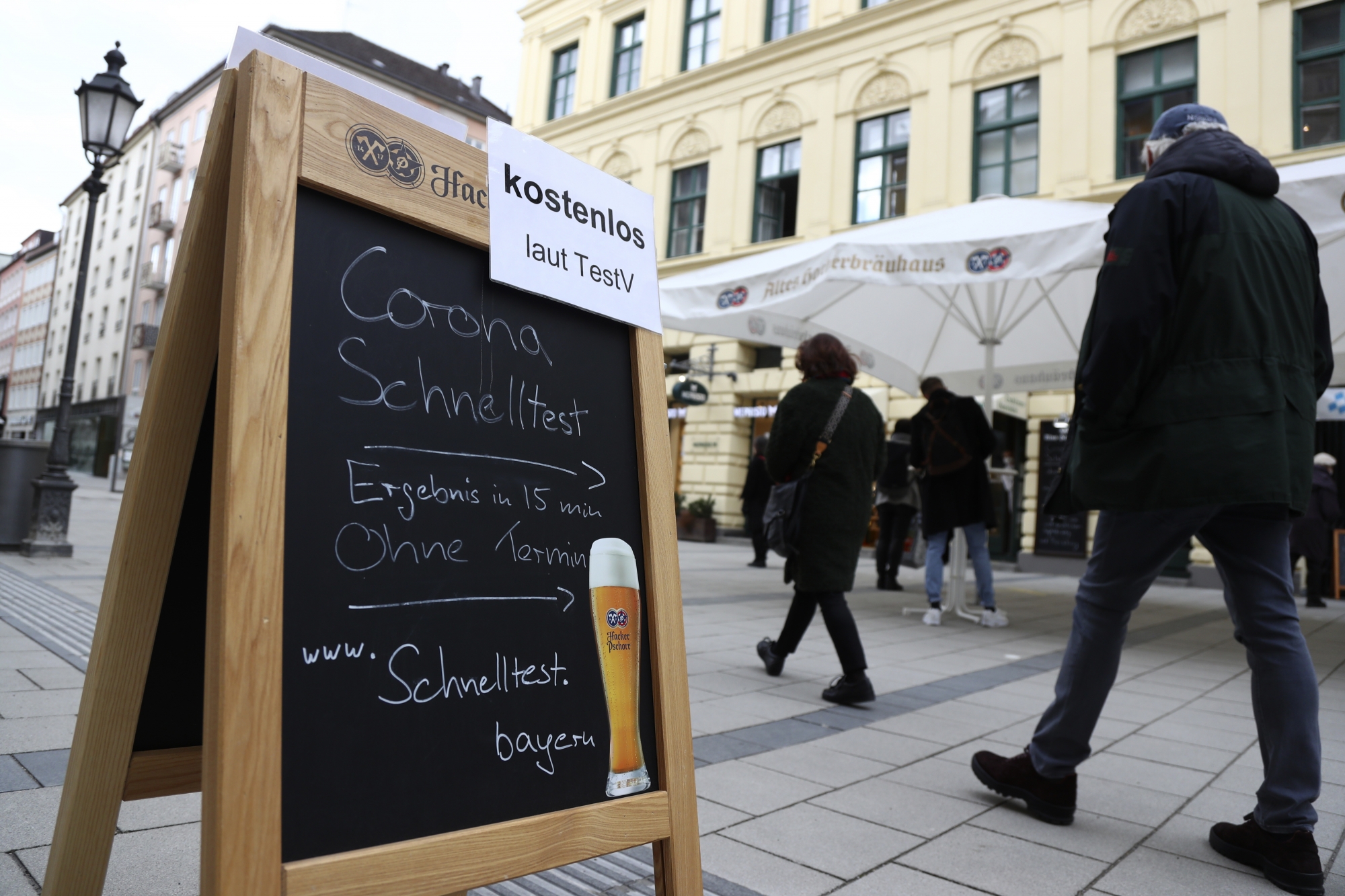 People pass the traditional Bavarian restaurant 'Hackerbraeuhaus' where a corona test center now works for SARS CoV-2 rapid tests downtown in Munich, Germany, Tuesday, March 23, 2021. (AP Photo/Matthias Schrader)