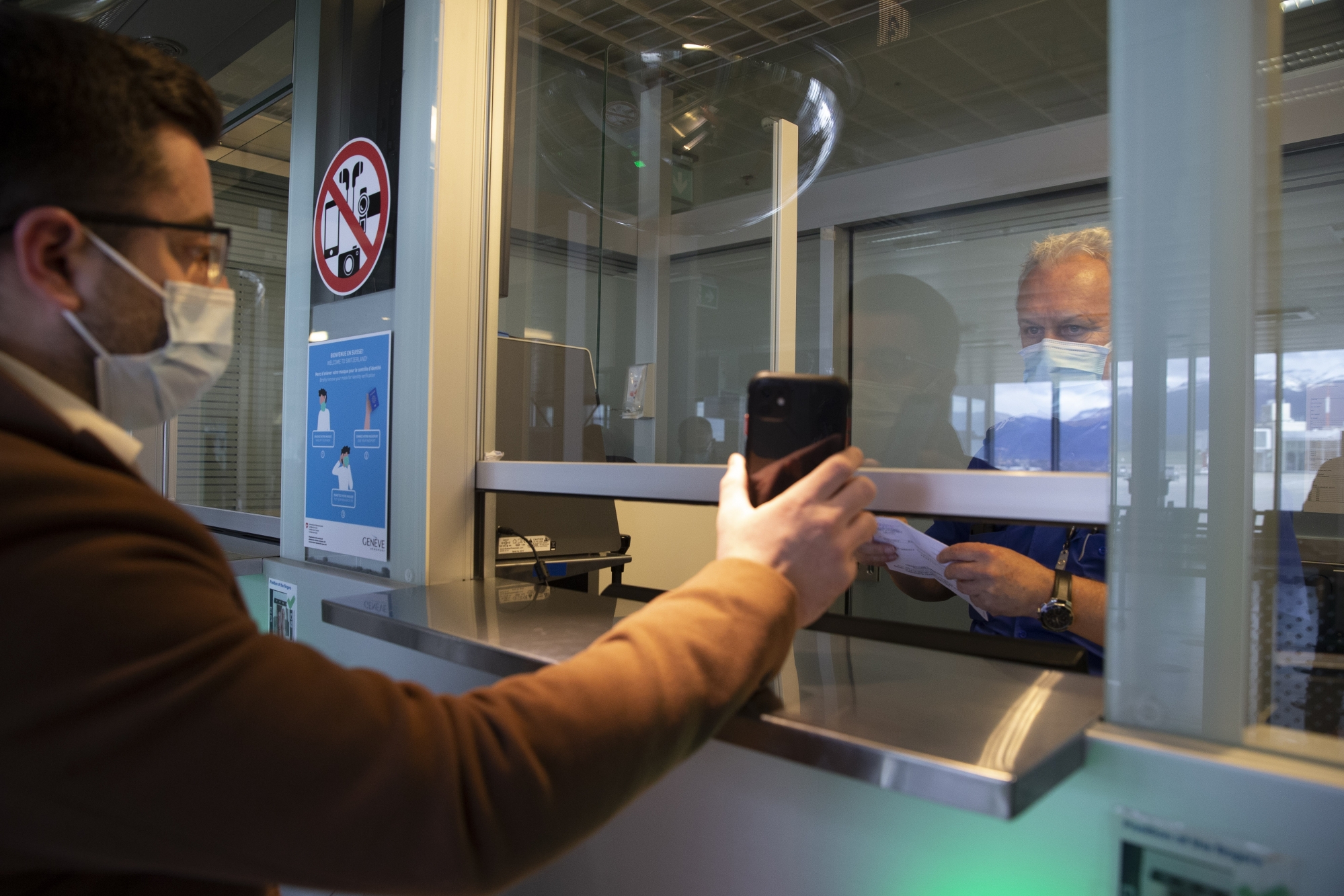 A Swiss border guard controls a passenger at the Swiss border crossing at the Geneve Aeroport as part of the new circulation arrangements put in place within the European Area to fight against the spread of coronavirus COVID-19, in Geneva, Switzerland, Monday, February 8, 2021. (KEYSTONE/Salvatore Di Nolfi)