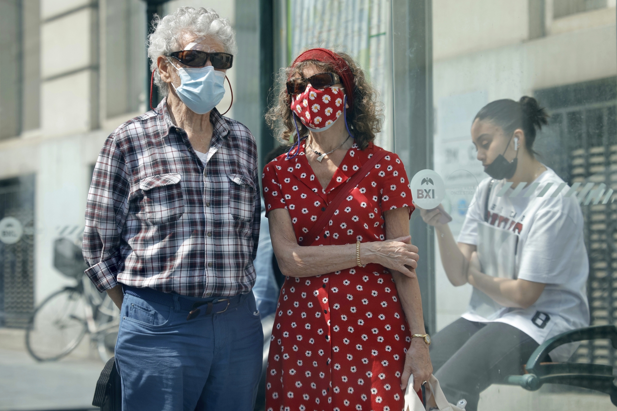 Two people wear protective face masks as they stand near a bus stop in Brussels, Wednesday, June 9, 2021. Belgians ventured out more widely Wednesday as the government lifted a raft of coronavirus restrictions. While the obligatory outdoor mask requirement for Brussels has been lifted some people were still cautious. (AP Photo/Olivier Matthys)