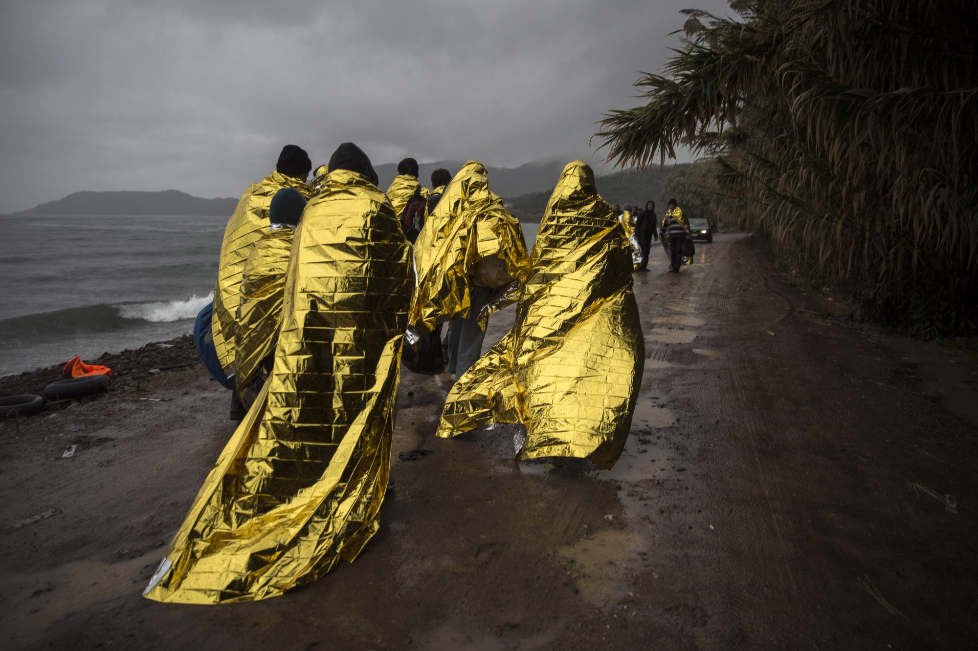 Refugees and migrants are covered with thermal blankets after their arrival on a dinghy from the Turkish coast to the Skala Sykaminias village on the northeastern Greek island of Lesbos, Friday, Oct. 23, 2015. The International Office for Migration says Greece over the last week experienced the largest single weekly influx of migrants and refugees this year, at an average of some 9,600 per day. (AP Photo/Santi Palacios)