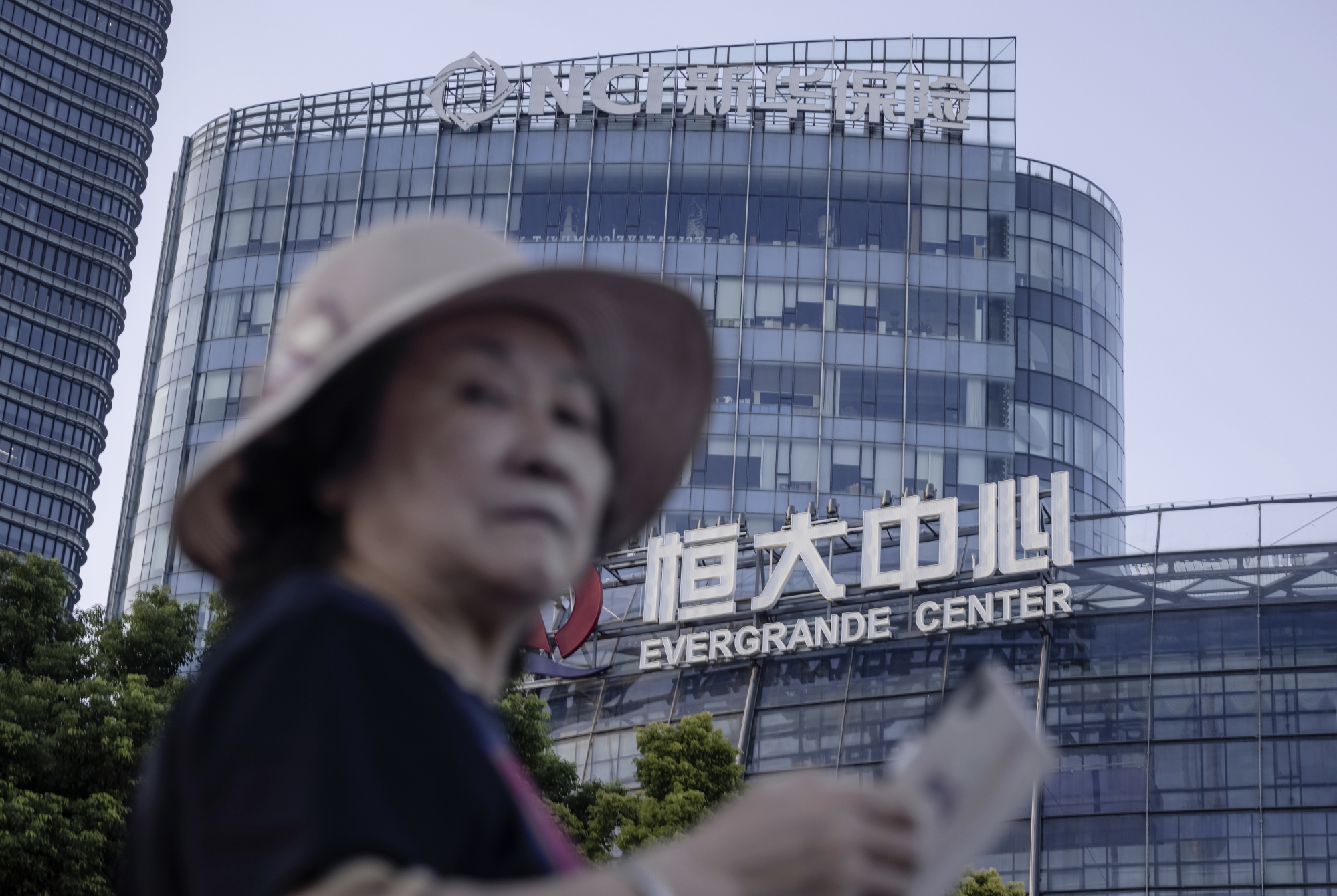 epa09479218 A woman walks past the Evergrande Center in Shanghai, China, 21 September 2021. Evergrande Group is China?s real estate conglomerate and the world?s most indebted property developer. Stock markets in Asia, the USA, and Europe were hit by a major sell-off on 20 September since the company?s shares closed 10 percent lower in Hong Kong. The Evergrande Group announced its concern in a stock filing this month that the group might not be able to meet its financial obligations.  EPA/ALEX PLAVEVSKI