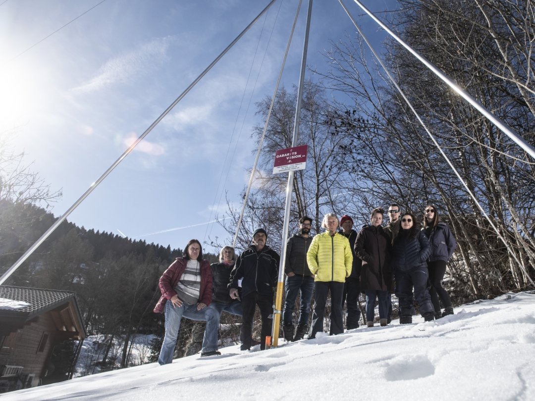 Plusieurs opposants à l'antenne Swisscom posent devant le gabarit situé à quelques mètres de chalets comme en aperçoit un à gauche.