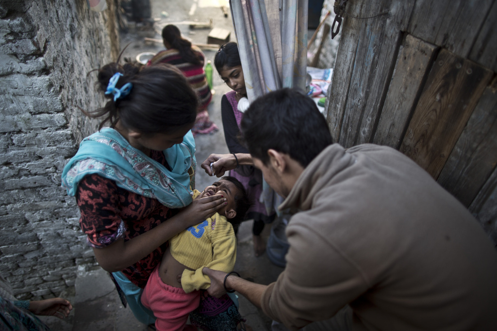 Pakistani health worker, Nooman Mehboob, 21, right, gives a child a polio vaccine, in Islamabad, Pakistan, Monday, Nov. 25, 2013. On Saturday, militants kidnapped four school teachers who were working on a polio vaccination drive in Khyber's Sipah village, said local government official Khurshid Khan. Negotiations are underway for their release, he said. Militants have killed over a dozen polio workers and police protecting them over the last year and they claim the workers are spies and the vaccination is meant to make Muslim children sterile. (AP Photo/Muhammed Muheisen)