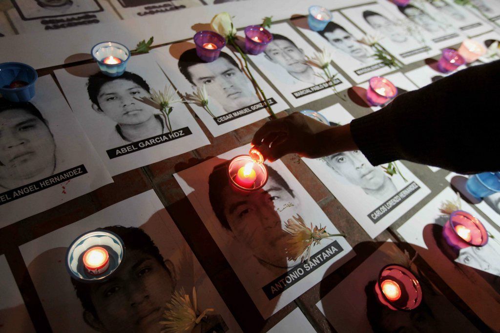 epa04497484 A demonstrator lights candles put over the images of 43 missing Mexican students during a solidarity protest demanding justice for the victims in Lima, Peru, 20 November 2014. Three demonstrations were taking place in the Mexican capital, led by students and parents of the 43 youngsters from Ayotzinapa teacher's training college who went missing from the city of Iguala, in the southern Mexican state of Guerrero on September 26. The authorities believe they were killed, but their bodies have yet to be found.  EPA/PAOLO AGUILAR