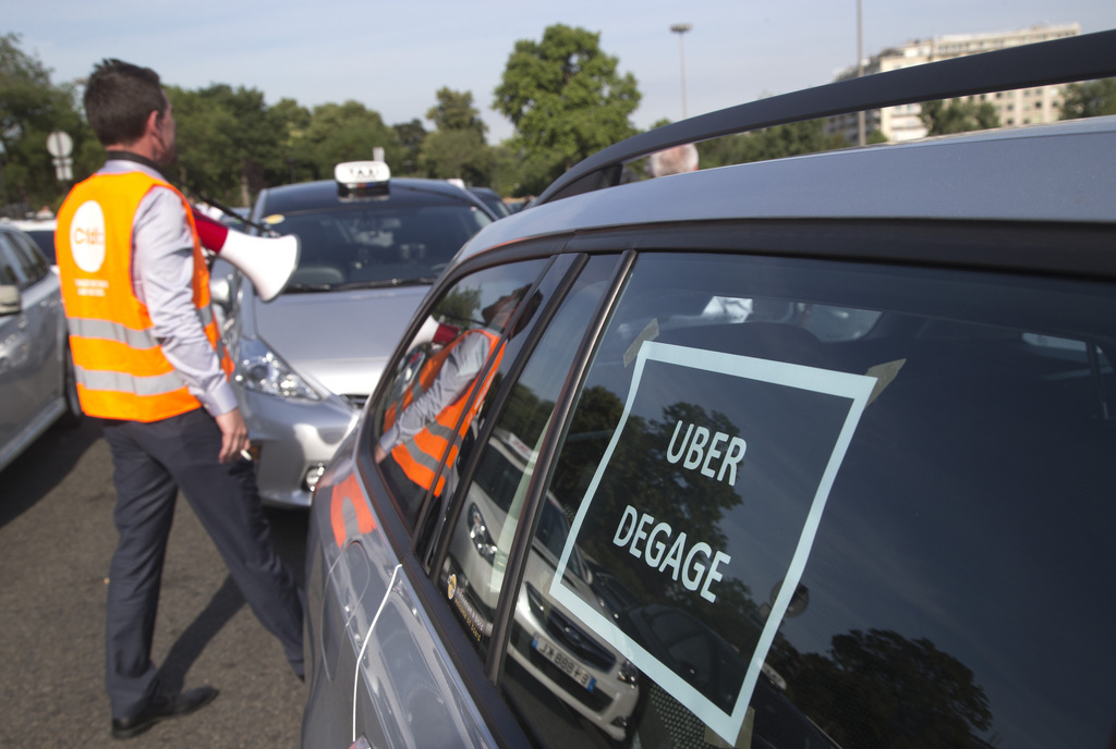 A taxi driver walks past a cab with  a poster reading "Uber go out" during a demonstration in Paris, Thursday, June 25, 2015 in Paris. French taxis are on strike around the country, snarling traffic in major cities and slowing access to Paris' Charles de Gaulle airport after weeks of rising and sometimes violent tensions over Uber. (AP Photo/Michel Euler)