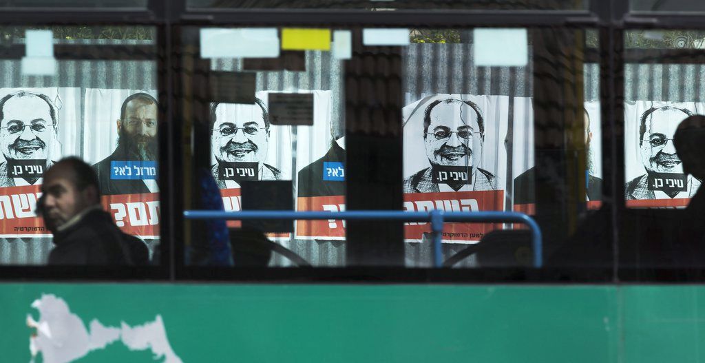epa04644357 An Israeli passenger bus passes election posters supporting far right-wing candidate Baruch Marzel (seen in color) opposite a black and white drawing of Ahmed Tibi a long-standing Israeli Arab lawmaker who is running on the United Arab list, in Jerusalem, 02 March 2015. The poster says in Hebrew, 'Marzel No, Tibi Yes. Are you Guys Nuts?' Israeli go to the polls in a general election on March 17 and if the United Arab list does well, could well act as 'king maker' in putting together the next coalition government, as a recent poll gives them some 12 seats in the next Knesset (Parliament).  EPA/JIM HOLLANDER