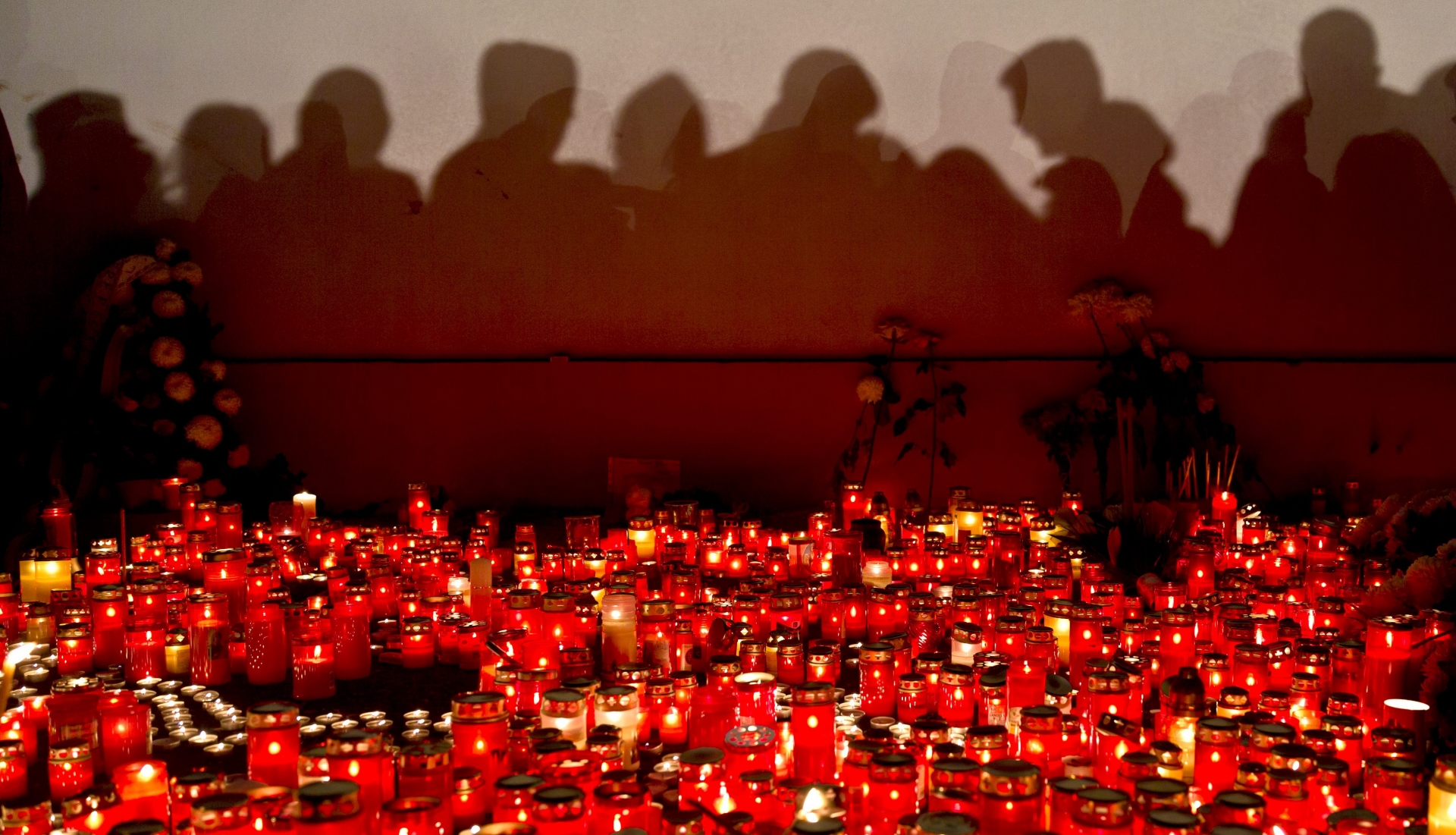 People cast shadows on a wall as they wait to light candles and lay flowers outside the compound that housed the nightclub where a fire occurred in the early morning hours in Bucharest, Romania, Saturday, Oct. 31, 2015. Hundreds of young people had gone clubbing at the hip Colectiv nightclub Friday night to enjoy a free concert by the Goodbye to Gravity metal band but the evening ended in horror, as the inferno caused a panic that killed tens of people and injured many others.(AP Photo/Vadim Ghirda)