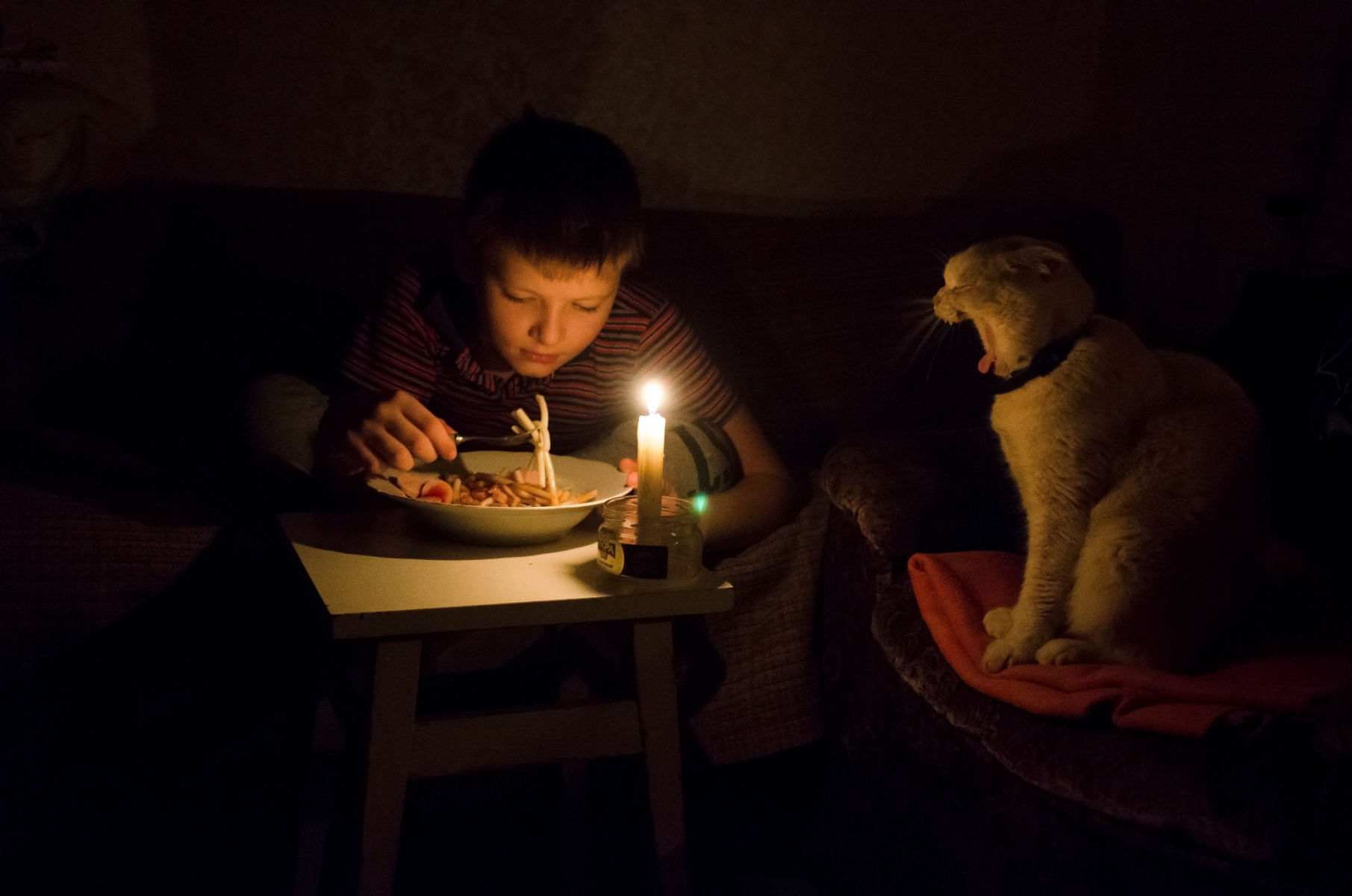 Nikita Alyabyev, 8, has dinner by candlelight with his cat at home in Simferopol, Crimea, Monday, Nov. 23, 2015. Two electricity transmission towers in Ukraine were damaged by explosions, leaving most of the nearly 2 million people on the disputed Crimean Peninsula without power on Sunday. (AP Photo/Anton Volk) CRIMEA ELECTRICITY