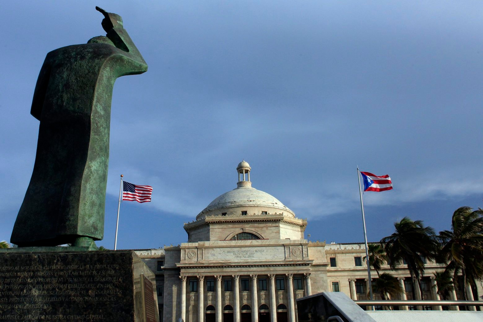 FILE - In this Wednesday, July 29, 2015, file photo, a bronze statue of San Juan Bautista stands in front of Puerto Ricoís Capitol as U.S. and Puerto Rican flags fly in San Juan, Puerto Rico. After months of pleading from the government of Puerto Rico, the U.S. Congress agreed on Wednesday, May 18, 2016, to help the territory restructure its massive public debt. (AP Photo/Ricardo Arduengo, File) PUERTO RICO DEBT CRISIS