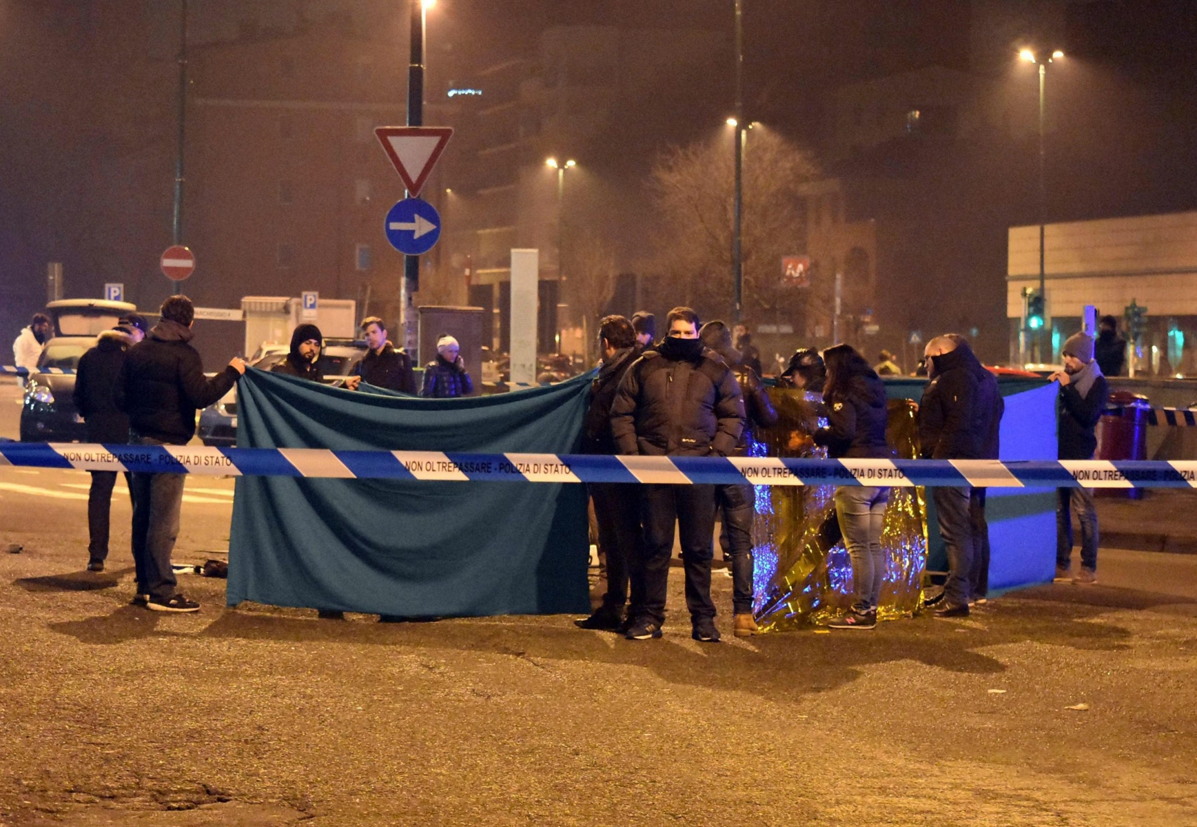 epa05686425 Italian police use blankets to prevent a direct view of a dead body at the sealed off scene of a shootout between police and a man in Milan's Sesto San Giovanni neighborhood, early 23 December 2016. Italy's Interior Minister Marco Minitti meanwhile has confirmed that the identity of the individual shot dead after a gunfight with Italian police this morning near Milan is Anis Amri, the 24 year old Tunisian suspected of the 19 December Berlin Christmas Market terrorist truck attack, that left at least 12 people dead and around 50 others injured.  EPA/DANIELE BENNATI ITALY BERLIN CHRISTMAS MARKET ATTACK