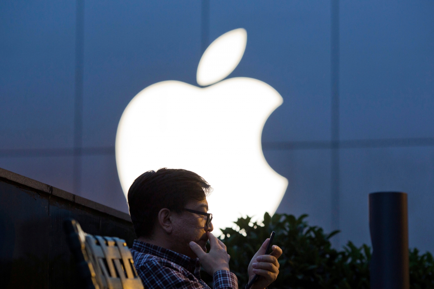FILE - In this May 13, 2016 file photo, a man uses his mobile phone near an Apple store logo in Beijing, China. Apple Inc. has filed suit in China challenging Qualcomm Inc.Äôs fees for technology used in smartphones two years after Chinese regulators fined the chipmaker for its licensing practices. Two suits filed by the iPhone maker accuse Qualcomm of abusing its control over essential technology to charge excessive licensing fees, a Beijing court said on its microblog. (AP Photo/Ng Han Guan, File) China Apple Qualcomm
