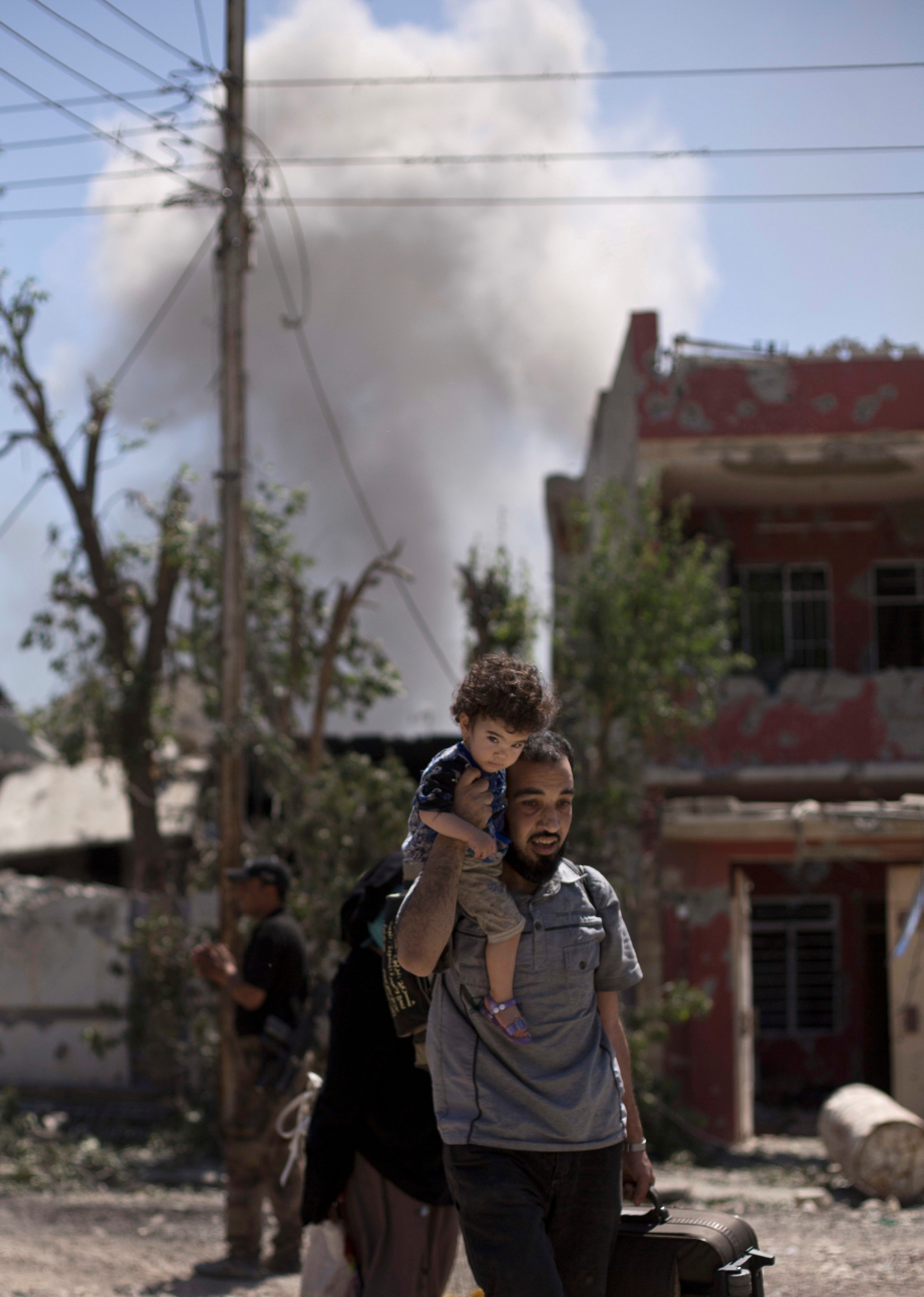 FILE - In this Wednesday, May 17, 2017 file photo, smoke from an airstrike rises as a man flees with a toddler during fighting between Iraqi special forces and Islamic State militants, in the al-Rifai neighborhood of western Mosul, Iraq. In Mosul, Iraqi forces are steadily closing in on remaining pockets of territory held by IS, but unlike past urban battles against them in Iraq, the militants still hunkered down in the city are mounting a stiff resistance, and the more the battle stretches out, the greater the risk for civilians remaining behind. (AP Photo/Maya Alleruzzo, File) Iraq Mosul Siege