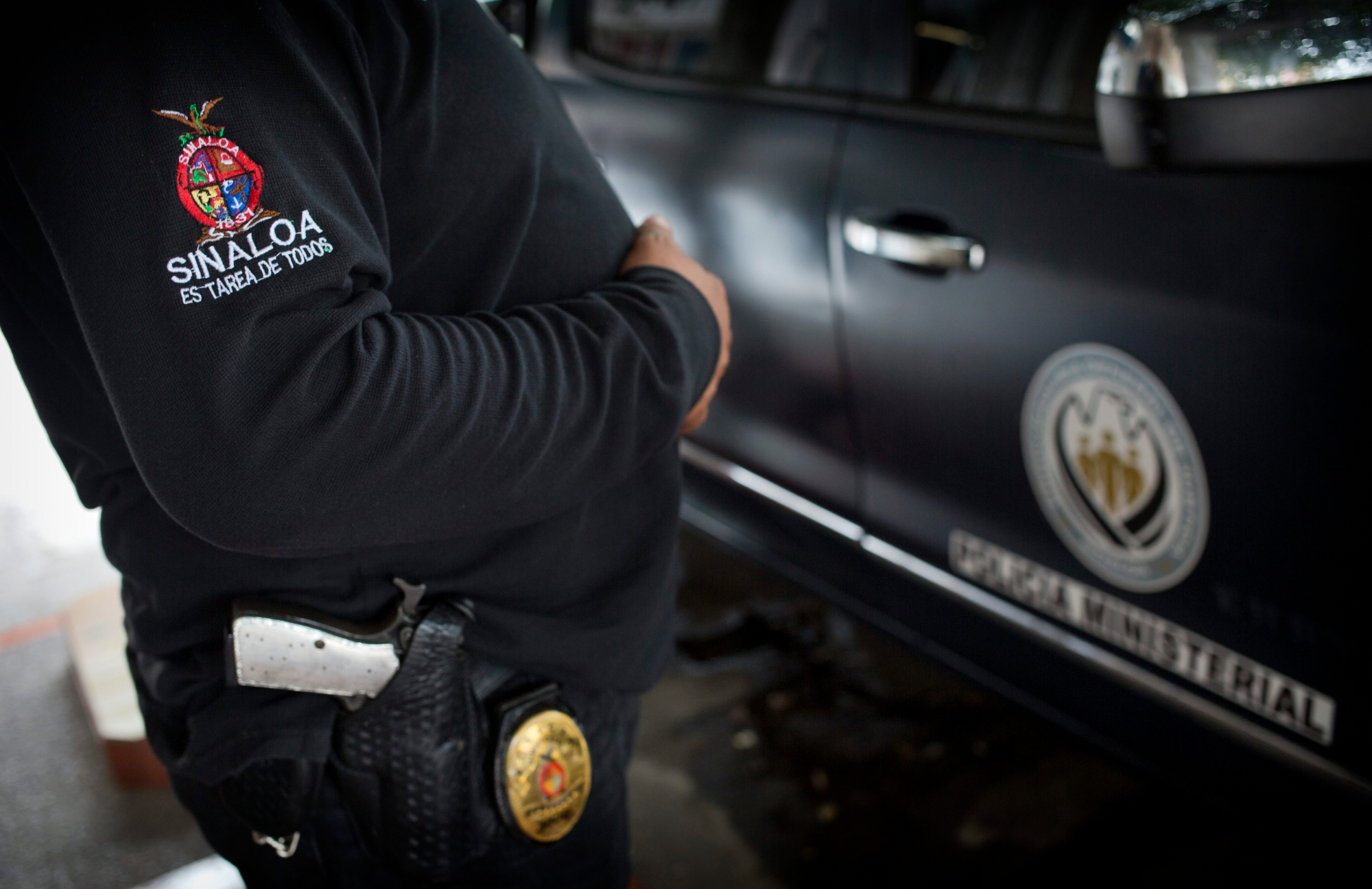 In this June 28, 2017 photo, a police officer stands outside Riodoce's office in Culiacan, Sinaloa state, Mexico. After the killing of Riodoce co-founder Javier Valdez, two police were assigned by the state government to guard the newspaper's offices. Half-jokingly, some of the reporters wondered whether these officers are among the 50 percent of cops whom the governor himself has said are not trustworthy. The badge on the police officer's sleeve reads, in Spanish, "Sinaloa is everyone's task." (AP Photo/Enric Marti) Mexico Journalists Under Fire