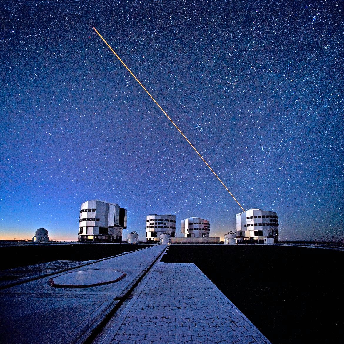 The ESO Very Large Telescope (VLT) during observations. In this picture, taken from the VLT platform looking north-northwest at twilight, the four 8.2-metre Unit Telescopes (UTs) are visible. From left to right, Antu, Kueyen, Melipal and Yepun, the Mapuche names for the VLT's giant telescopes. In front of the UTs are the four 1.8-metre Auxiliary Telescopes (ATs), entirely dedicated to interferometry, a technique which allows astronomers to see details up to 25 times finer than with the individual telescopes. The configuration of the ATs can be changed by moving them across the platform between 30 different observing positions. One of these positions is visible in the foreground, covered by a hexagonal pad. A reddish laser beam is being launched from UT4 (Yepun) to create an artificial star at an altitude of 90 km in the Earth´s mesosphere. This Laser Guide Star (LGS) is part of the Adaptive Optics system, which allows astronomers to remove the effects of atmospheric turbulence, produc