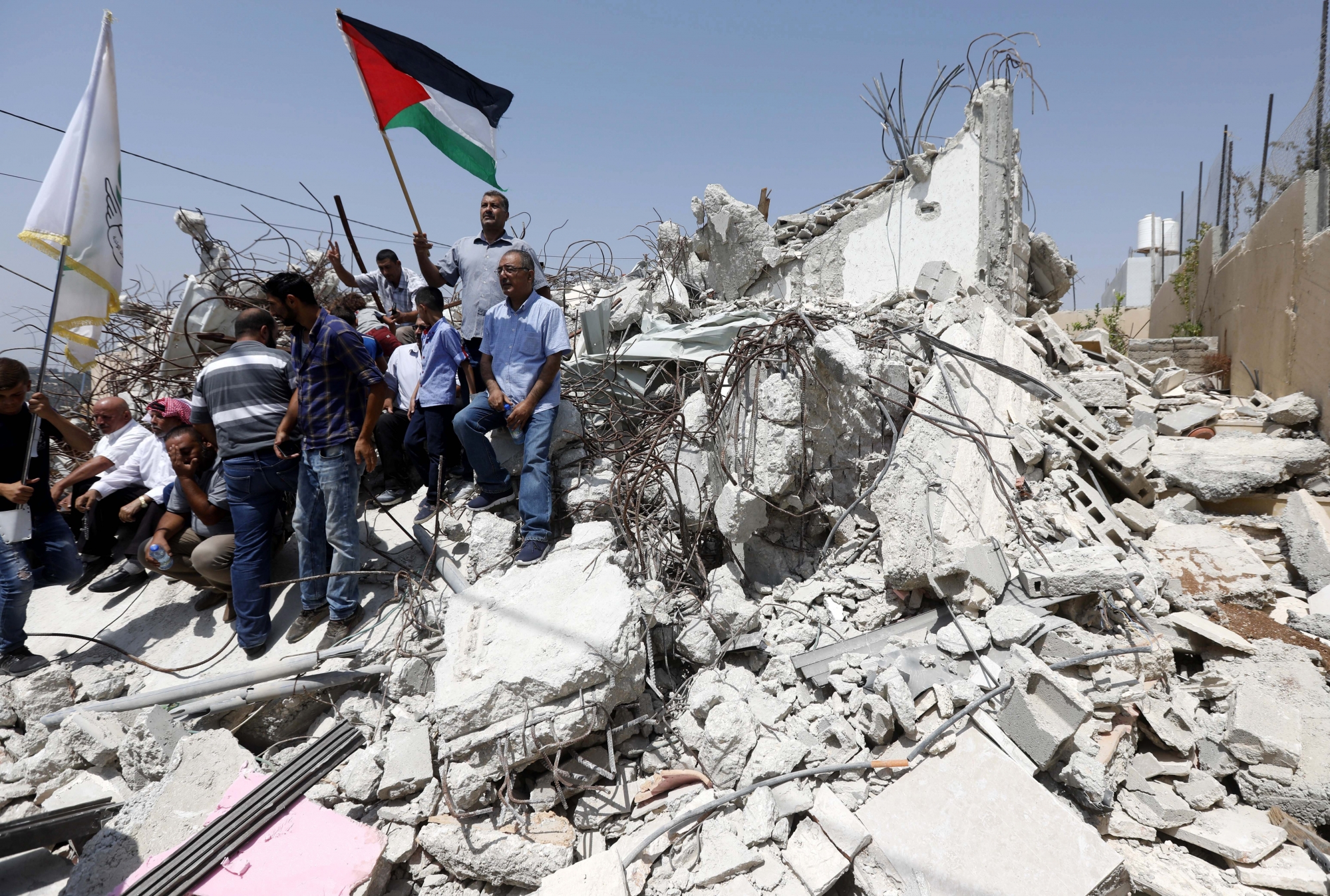 epa06162392 Palestinians hold flags on a house which was demolished in 2016, in the West Bank village of Walajeh, during a protest near Bethlehem, 25 August 2017. Palestinians protest against house demolishing in the village by the Israeli army, more than 20 houses received demolish notification by the Israeli army, that claimed they dont have the Israeli permits  needed to build in area C.  EPA/ABED AL HASHLAMOUN MIDEAST PALESTINIANS PROTEST