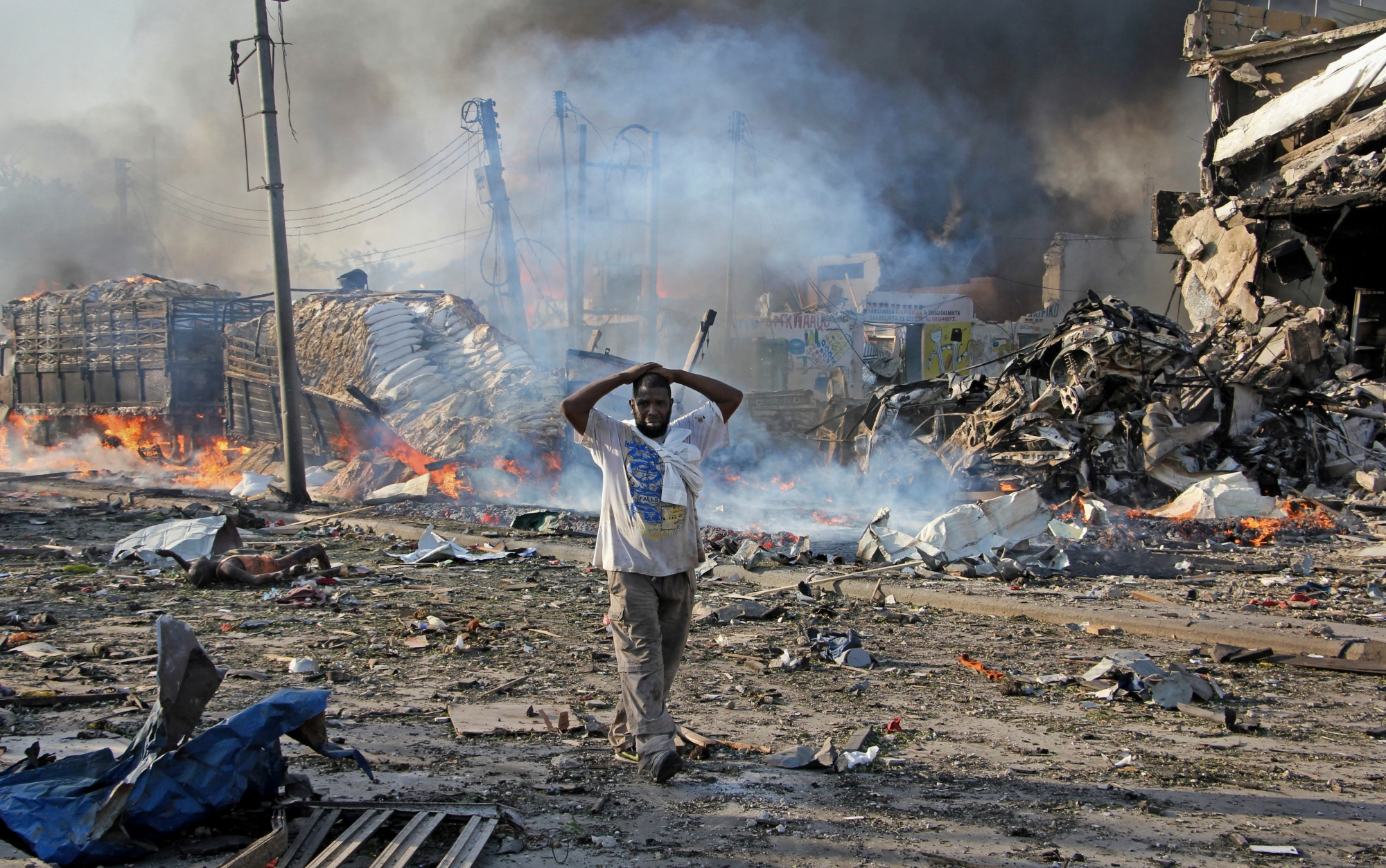 A Somali gestures as he walks past a dead body, left, and destroyed buildings at the scene of a blast in the capital Mogadishu, Somalia Saturday, Oct. 14, 2017. A huge explosion from a truck bomb has killed at least 20 people in Somalia's capital, police said Saturday, as shaken residents called it the most powerful blast they'd heard in years. (AP Photo/Farah Abdi Warsameh) Somalia Explosion