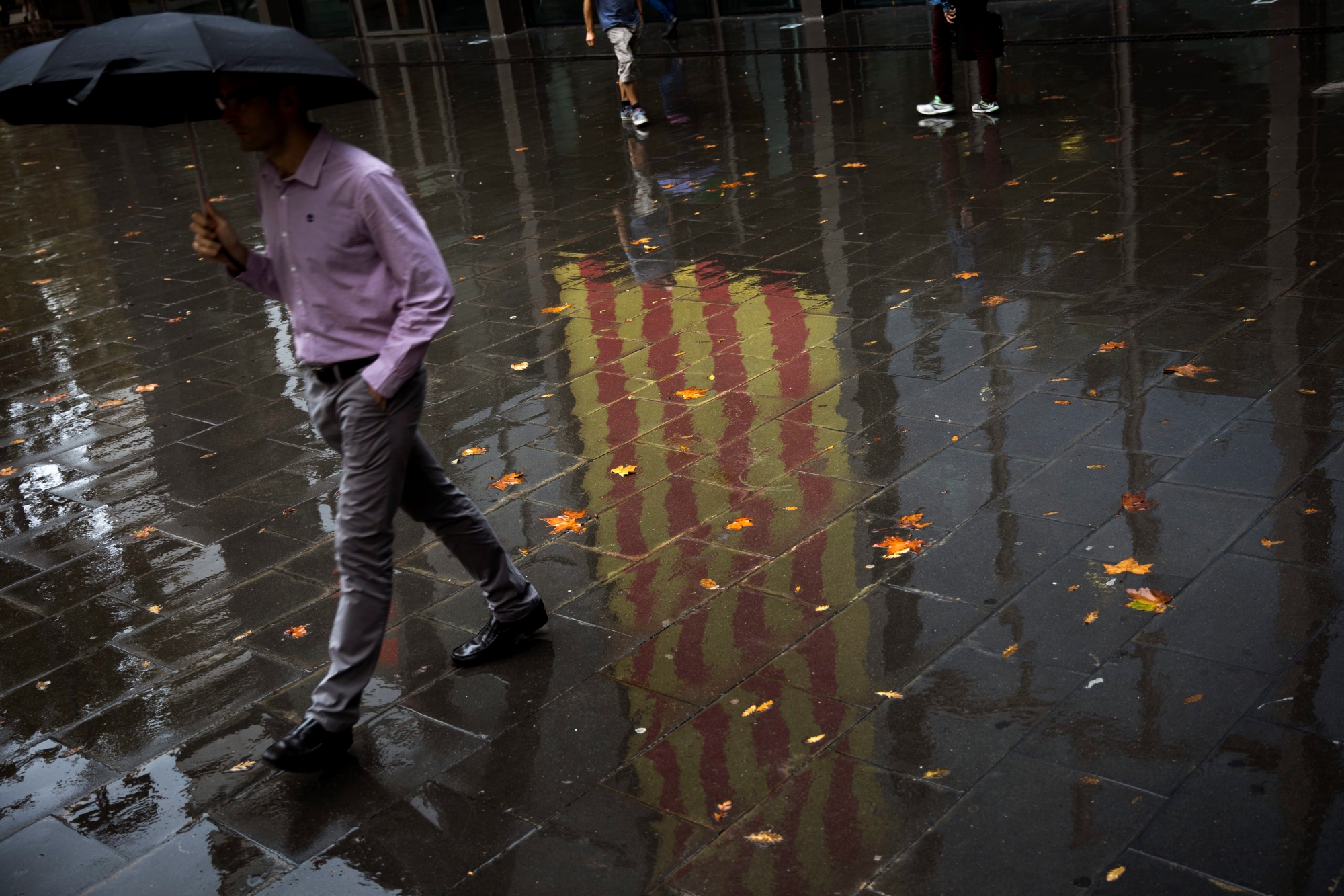 People walk past a Catalan flag reflected on the wet ground in Barcelona, Spain, Thursday, Oct. 19, 2017. Spain's government on Thursday immediately rejected a threat by Catalonia's leader to declare independence unless talks are held, calling a special Cabinet session for the weekend to activate measures to take control of the region's semi-autonomous powers. (AP Photo/Emilio Morenatti) Spain Catalonia