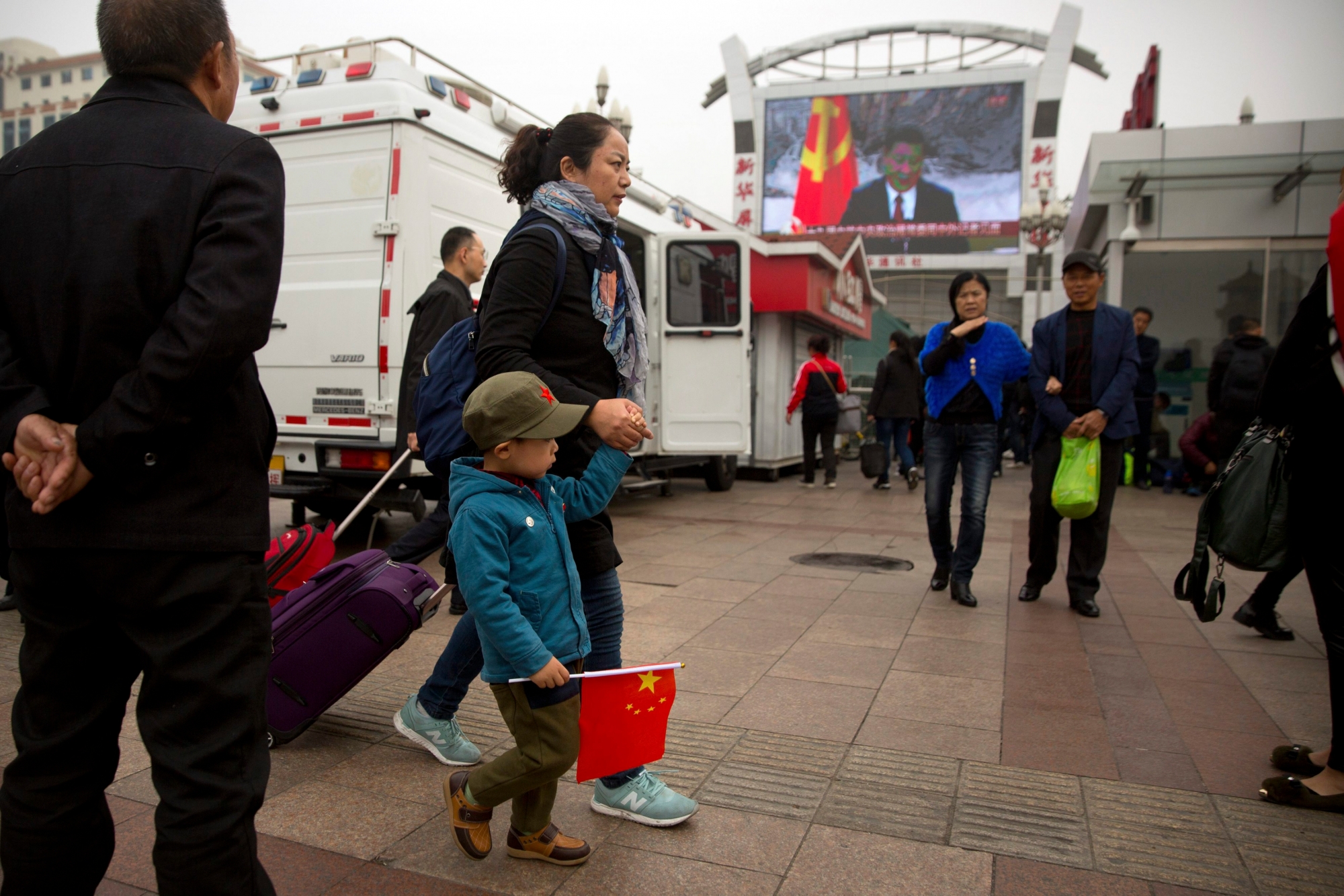 A woman and a boy carrying a Chinese flag walk past a television screen outside of the Beijing Railway Station showing a live broadcast of Chinese President Xi Jinping introducing members of the Politburo Standing Committee of China's 19th Party Congress at the Great Hall of the People in Beijing, Wednesday, Oct. 25, 2017. Communist Party leader Xi Jinping on Wednesday unveiled the lineup of the party's highest body who will rule alongside him as he embarks on a second five-year term as party leader. (AP Photo/Mark Schiefelbein) China Party Congress