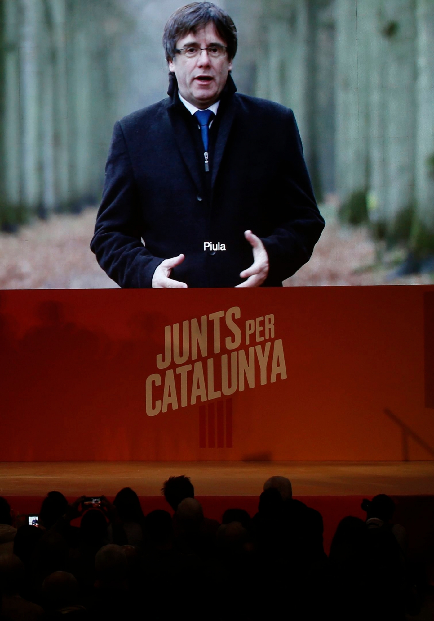 Ousted Catalan president Carles Puigdemont appears on a giant screen during an event of his political platform 'Junts per Catalunya' to mark the official start of the electoral campaign for the Catalan regional election in Barcelona, Spain, Monday, Dec. 4, 2017. Campaigning officially begins at midnight Monday, and in the hours before that moment Catalan pro-independence groups hope to stage protests in front of town halls across the region against the Supreme Court's decision on the detained separatists. (AP Photo/Manu Fernandez) Spain Catalonia