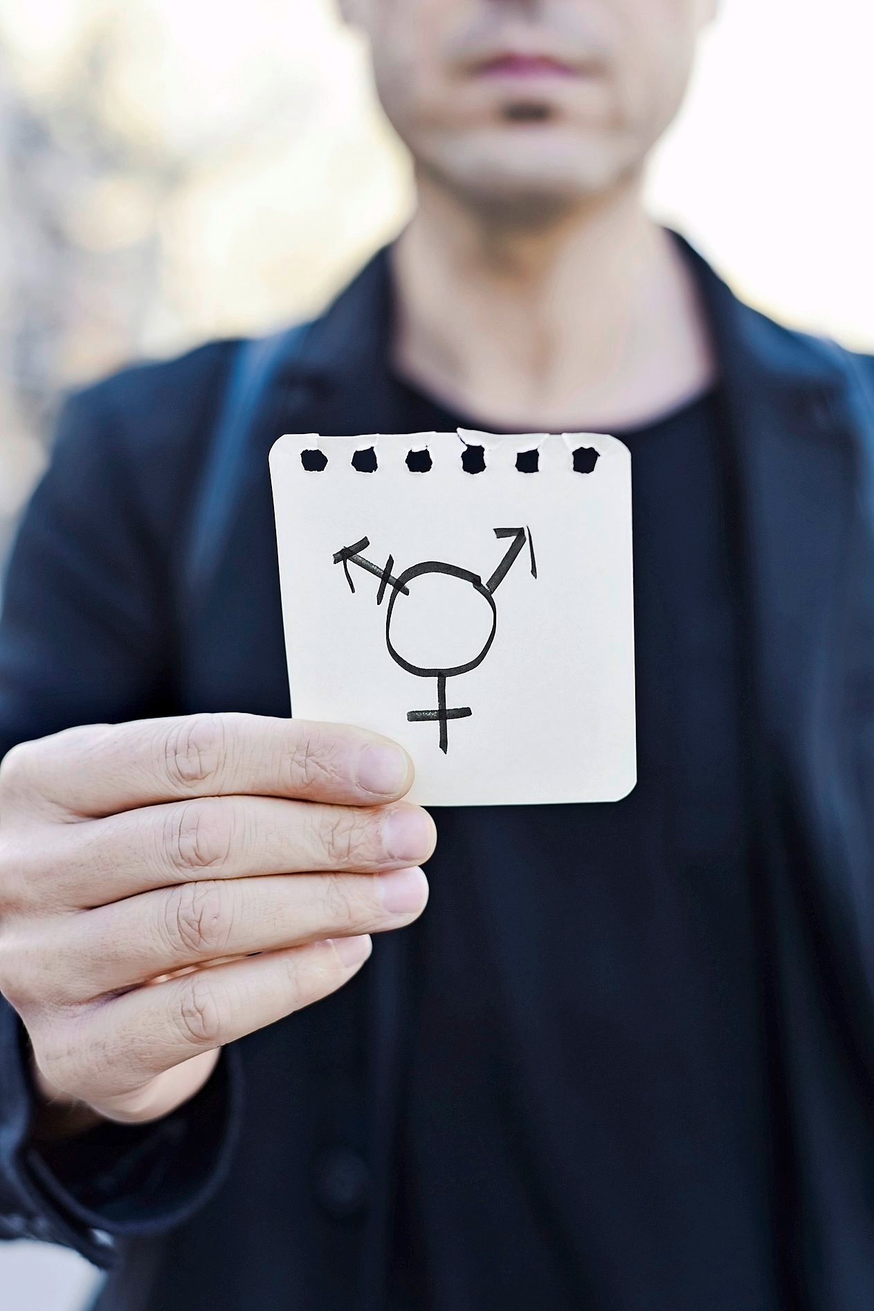 closeup of a young Caucasian man in the street showing a piece of paper with a transgender symbol drawn in it man and transgender symbol