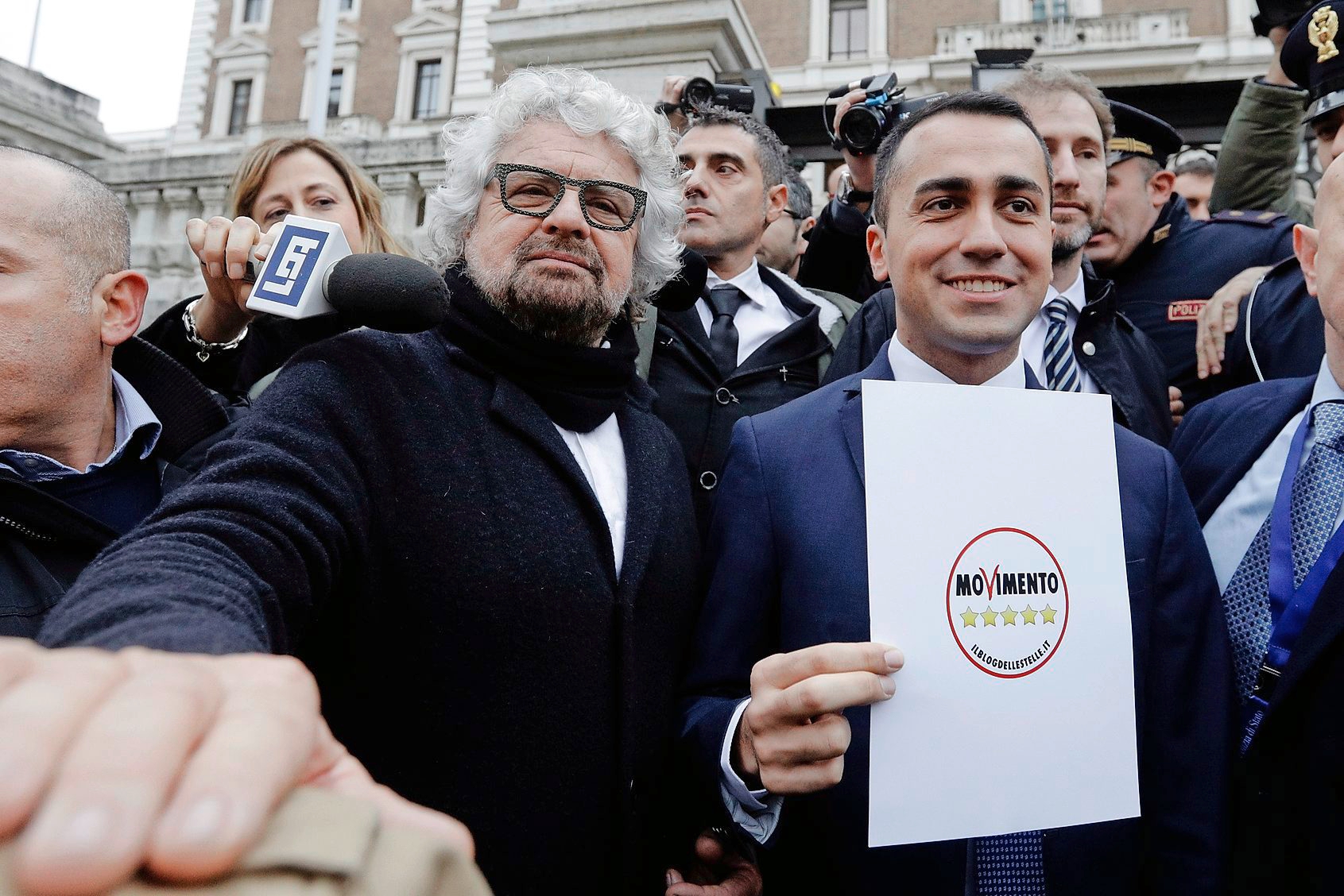 5-Star Movement party lawmaker Luigi Di Maio, center, flanked by movement founders Beppe Grillo, left, and Davide Casaleggio, right, holds the official party symbol which they registered for the upcoming elections, outside the Italian Interior Ministry building, in Rome, Friday, Jan. 19, 2018. Italians vote March 4 in a parliamentary election, the vote is shaping up into a three way race between a weakened Democratic Party, the populist 5-Star Movement and the center-right, with Salvini's League vying for dominance with former Premier Silvio Berlusconi's Forza Italia. (AP Photo/Gregorio Borgia) Italy Elections