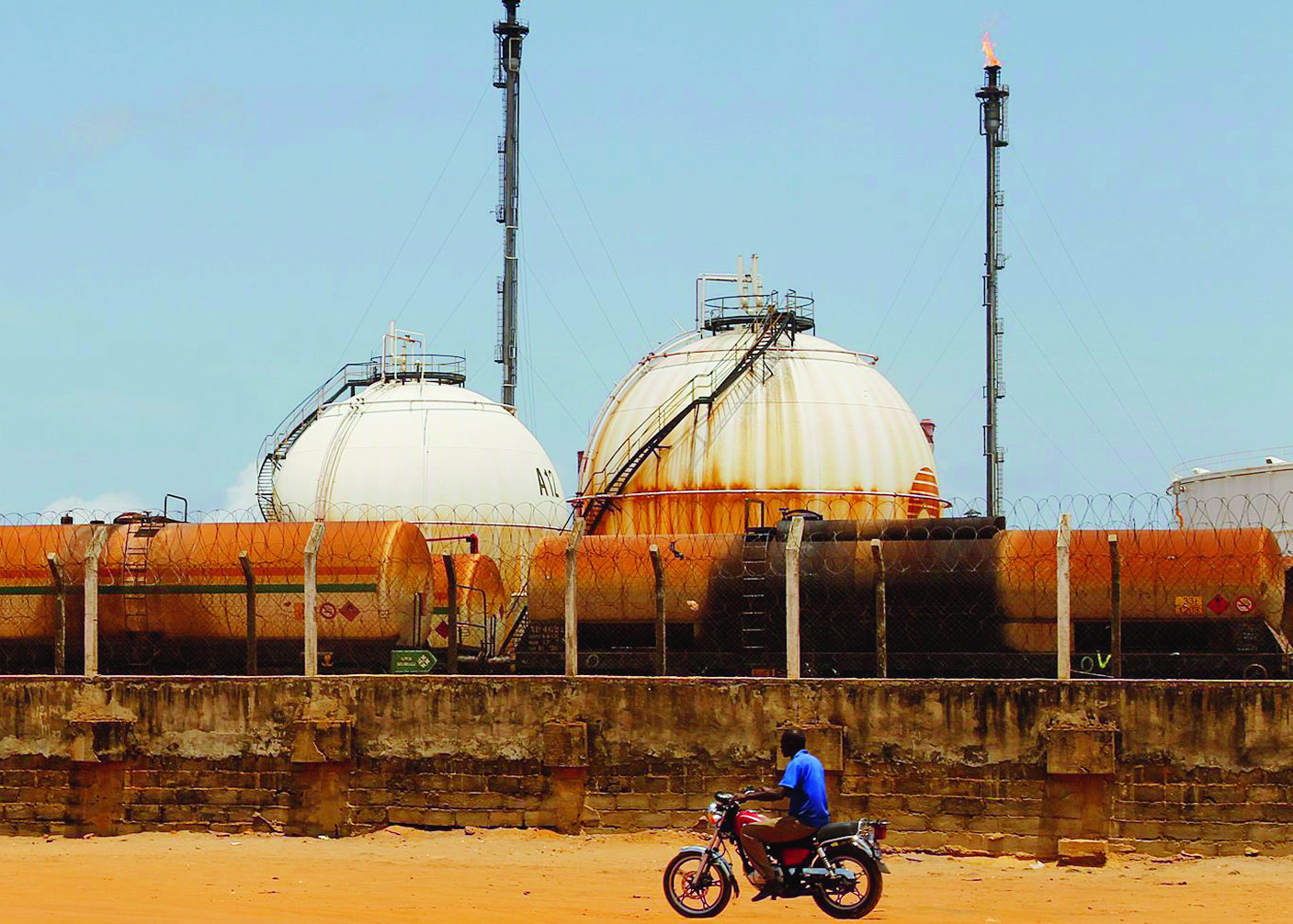 epa05281730 A photograph made available 28 April 2016 shows a motorcyclist riding in front of the Ivorien Society of Refinage facility (Société Ivoirienne de Refinage (SIR) in Abidjan, Ivory Coast 26 April 2016. According to global energy consultancy group Wood Mackenzie Africa's place as a significant producer and net exporter of oil in the world is forecast to grow to 15 per cent by 2020 due to new discoveries in West Africa. Substantial growth potential exists in West Africa with 40 billion barrels of discovered but undeveloped reserves and 55 billion barrels of yet-to-find oil. Since Jubilee discovery in 2007 companies are exploring other parts of the region between Ghana to Mauritania looking for analogous Cretaceous turbidite prospects. Offshore explorations in Sierra Leone and the Ivory Coast are high potential areas for investment beyond that of Nigeria and Angola.  EPA/LEGNAN KOULA ELFENBEINKUESTE BENZIN