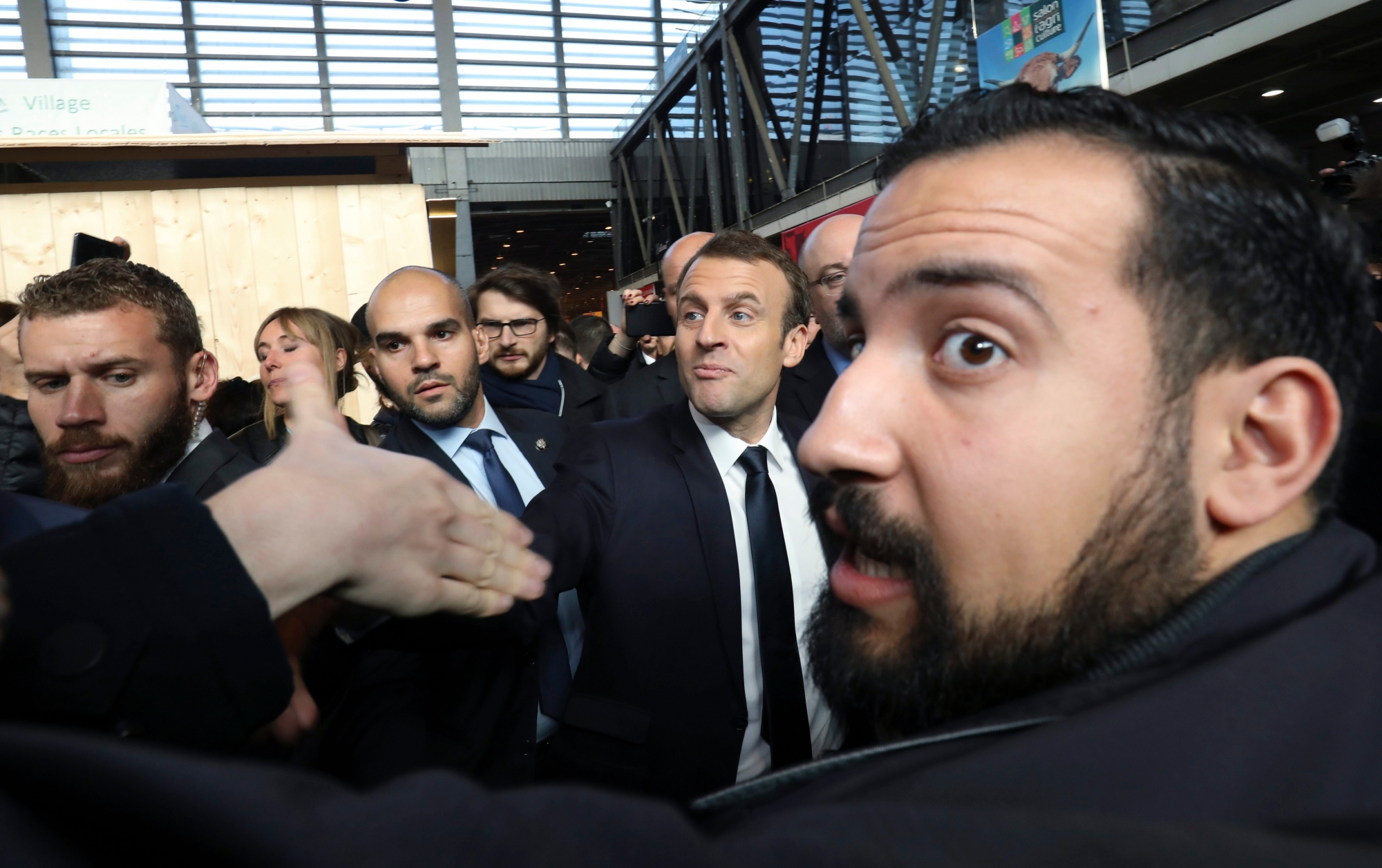 epa06906477 French president Emmanuel Macron (C) shakes hands as the Elysee senior security officer Alexandre Benalla (R) looks on during a visit at the 55th International Agriculture Fair (Salon de l'Agriculture) at the Porte de Versailles exhibition center in Paris, France, 24 February 2018 (issued on 23 July 2018). A video has been released on 19 July 2018 allegedly showing Alexandre Benalla, the French President Emmanuel Macron's deputy chief of staff, wearing a riot helmet and police uniform while attacking protesters during street demonstrations on 01 May 2018.  EPA/LUDOVIC MARIN / POOL MAXPPP OUT FRANCE GOVERNMENT ELYSEE SECURITY OFFICER SCANDAL