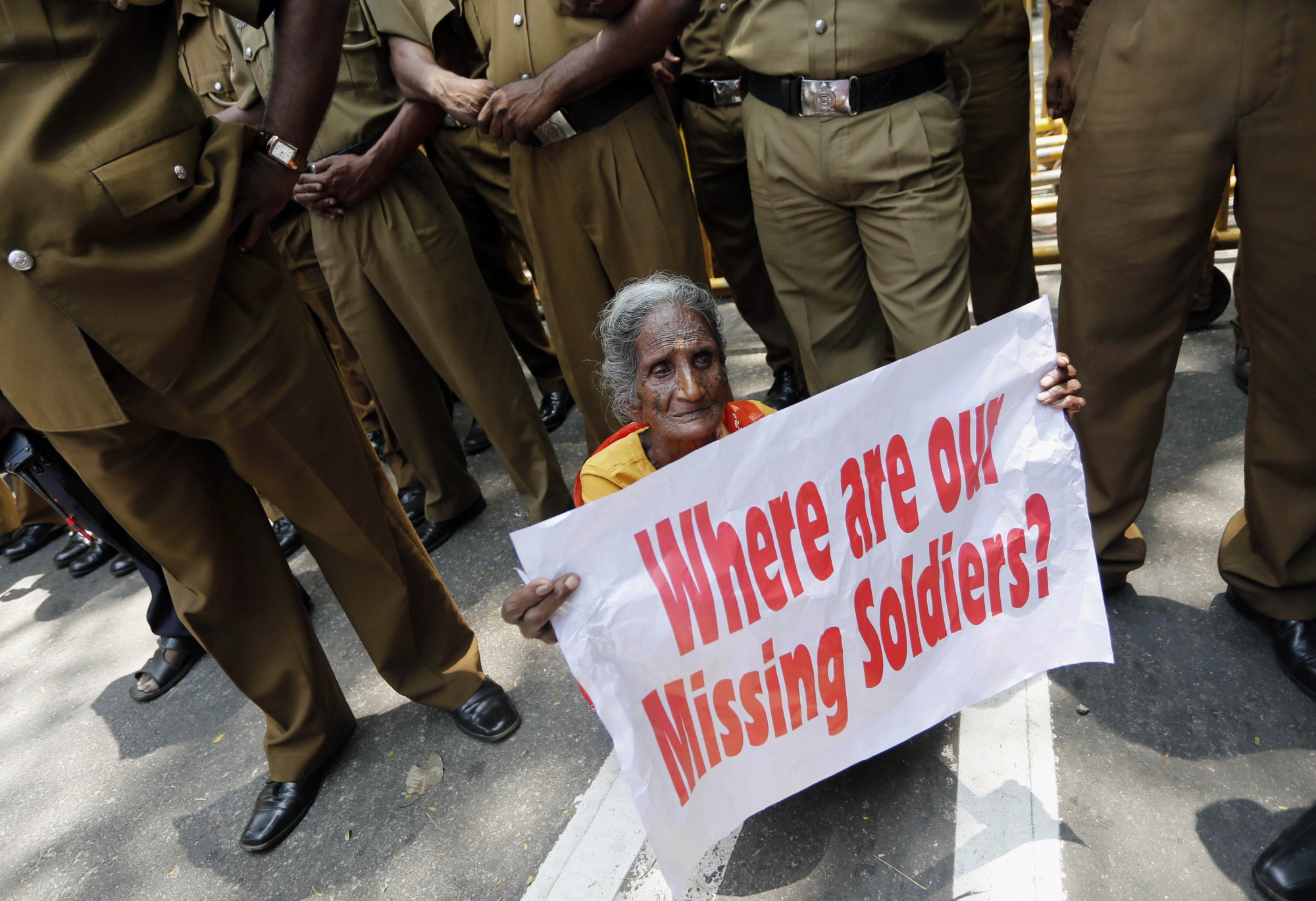 A Sri Lankan ethnic Tamil woman supporting the Dead and Missing Personís Parents Front holds a placard as police officers stand guard during a protest in Colombo, Sri Lanka, Friday, Aug. 30, 2013. Hundreds of Sri Lankans protested Friday outside the country's United Nations office, urging the visiting human rights chief Navi Pillay to probe atrocities allegedly committed by the Tamil Tiger rebels during the nation's quarter century-long civil war.(AP Photo/Eranga Jayawardena) Sri Lanka UN