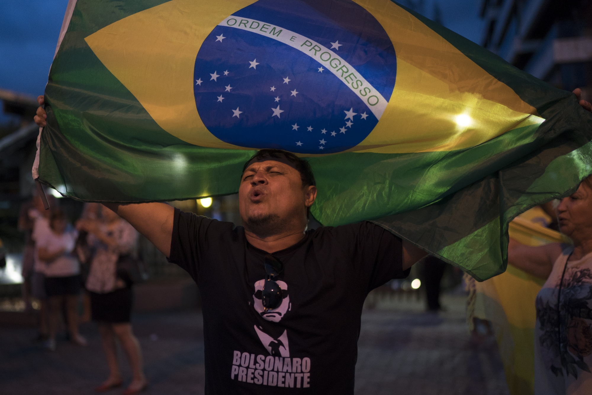 A man sing the Brazil's national anthem as he waves the national flag in support leading presidential candidate Jair Bolsonaro, outside Bolsonaro's residence in Rio de Janeiro, Brazil, Saturday, Sept. 29, 2018. Bolsonaro, who suffered intestinal damage and severe internal bleeding after the Sept. 6 attack at a campaign event and has undergone multiple surgeries, was discharged Saturday from a Sao Paulo hospital where he was being treated. (AP Photo/Leo Correa) Brazil Elections Bolsonaro
