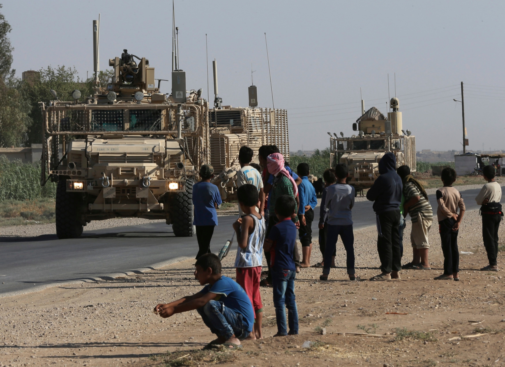 FILE - In this July 26, 2017, file photo, Syrians look at a U.S. armored vehicle convoy on a road that leads to Raqqa, northeast Syria. With Islamic State's near total defeat on the battle field, the extremist group has reverted to what it was before its spectacular series of conquests in 2014 _ a shadowy terror network that targets vulnerable civilian populations and exploits state weaknesses to incite on sectarian strife. But a recent surge in false claims of responsibility for attacks also signals that the group is struggling to stay relevant after losing its proto-state and its dominance of the international news agenda. (AP Photo/Hussein Malla, File) Islamic State