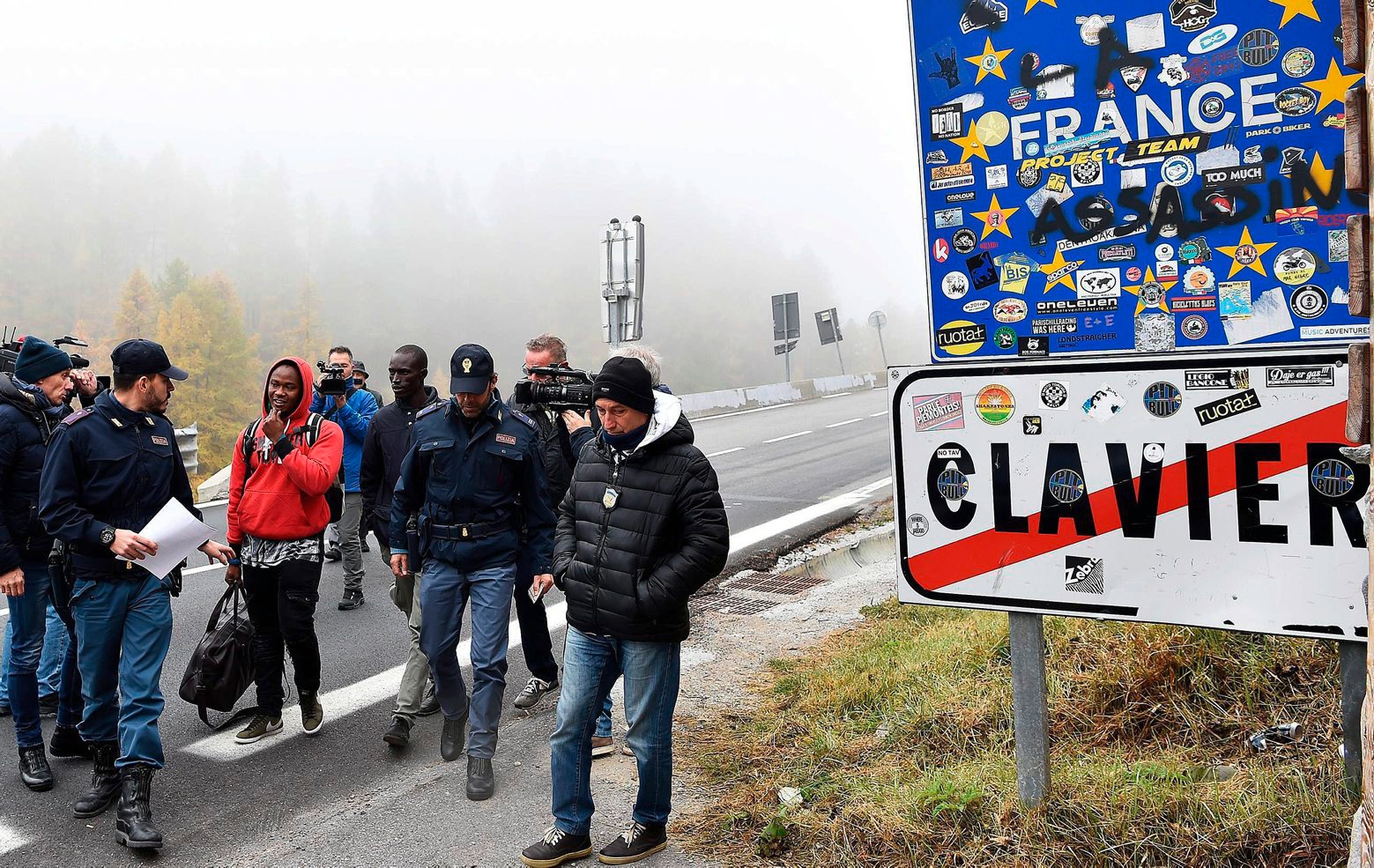 Reporters film men checked by Italian Police in Claviere, Italy, nearby the border between Italy and France, Monday Oct. 22, 2018.  Italy has started patrolling in Claviere after reports that a French police truck crossed the border and dropped off two presumed migrants in the woods near Turin before returning to France. (Alessandro Di Marco /ANSA via AP) Italy Europe Migrants