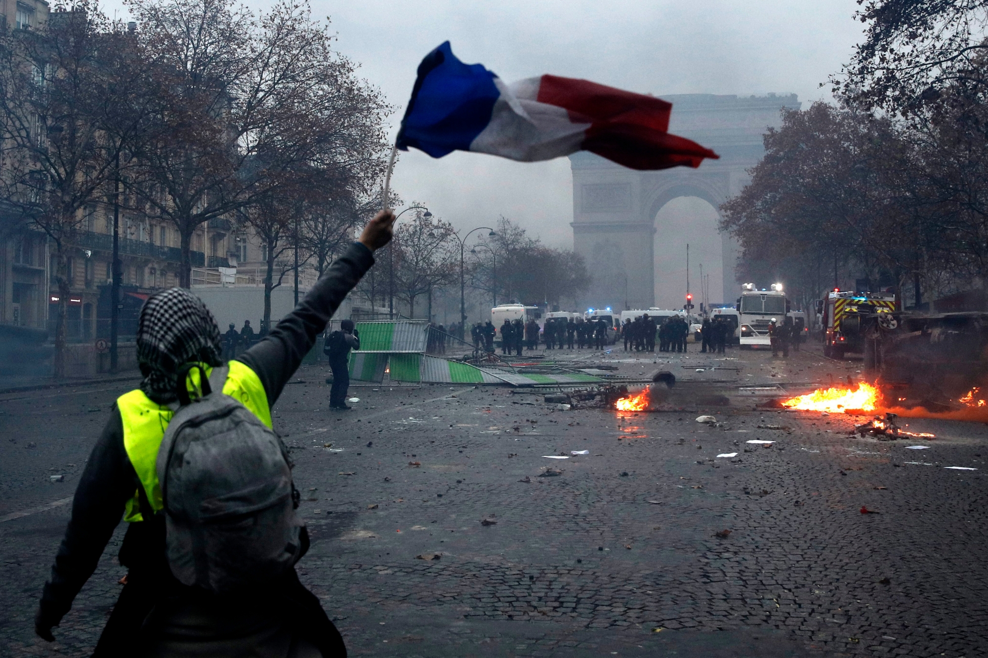 epa07202682 A protester wearing a yellow vest (gilets jaunes) waves a French flag during clashes with riot police near the Arc de Triomphe as part of a demonstration over high fuel prices on the Champs Elysee in Paris, France, 01 December 2018. The so-called 'gilets jaunes' (yellow vests) are a protest movement, which reportedly has no political affiliation, is protesting across the nation over high fuel prices.  EPA/YOAN VALAT FRANCE PROTEST FUEL TAXES