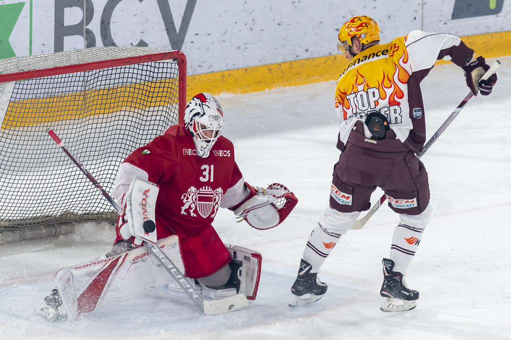 Le gardien lausannois, Sandro Zurkirchen, gauche, lutte pour le puck avec le joueur genevois, Tanner Richard, droite.