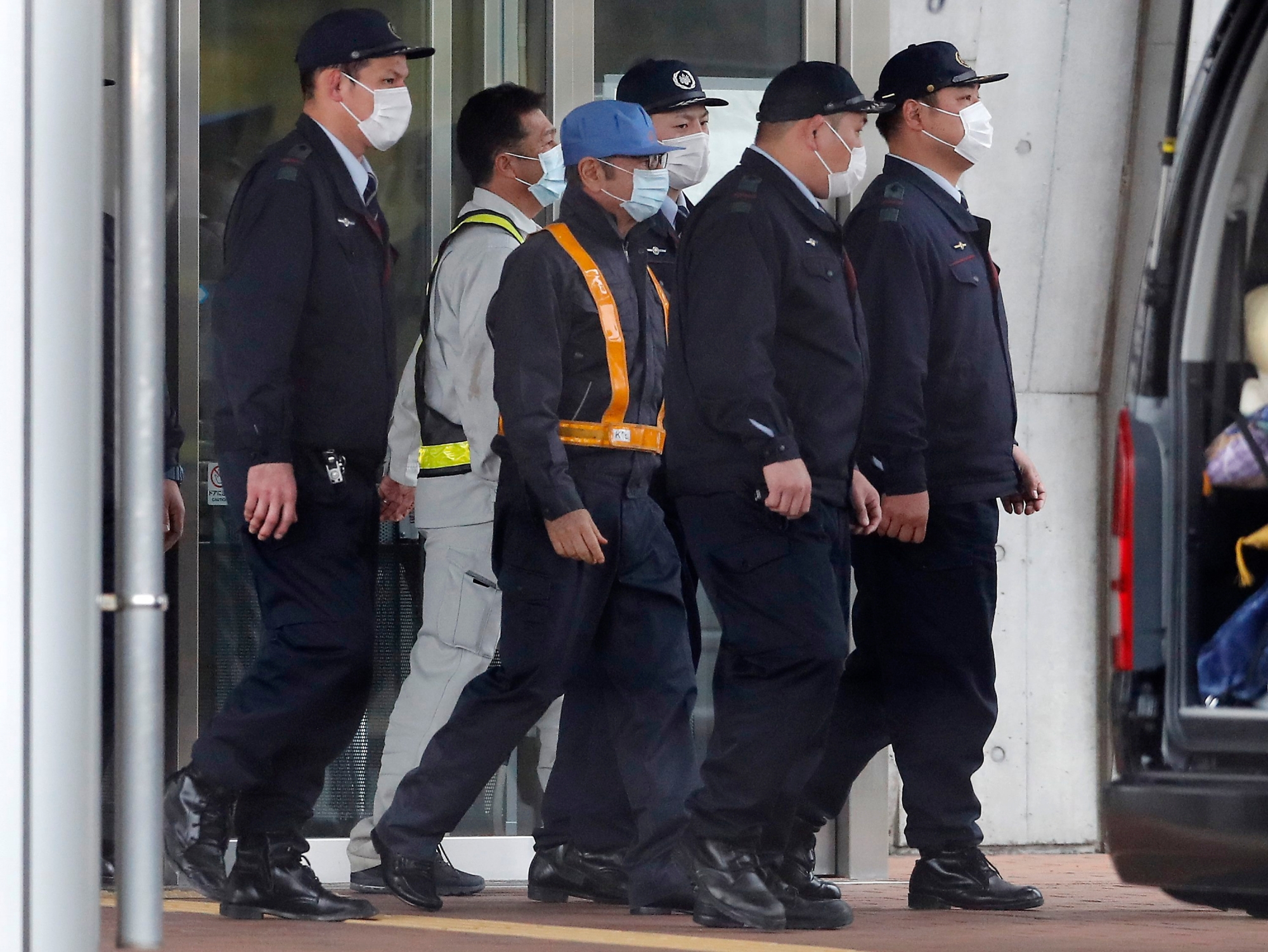 A masked man, center with blue cap, believed to be former Nissan Chairman Carlos Ghosn, walks out with security guards from Tokyo Detention Center in Tokyo Wednesday, March 6, 2019, after posting 1 billion yen ($8.9 million) in bail once an appeal by prosecutors against his release was rejected. (AP Photo/Eugene Hoshiko) Japan Nissan Ghosn