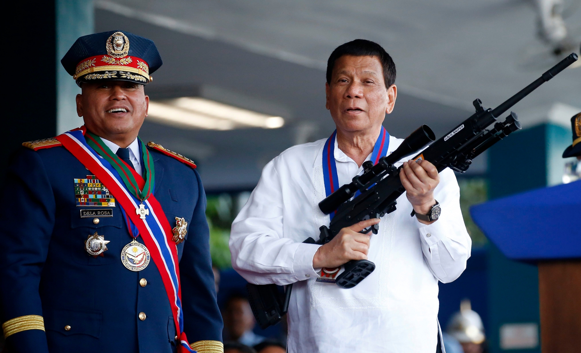 FILE - In this April 19, 2018 file photo, Philippine President Rodrigo Duterte, right, jokes to photographers as he holds an Israeli-made Galil rifle which was presented to him by former Philippine National Police Chief Director General Ronald Dela Rosa at the turnover-of-command ceremony at the Camp Crame in Quezon city northeast of Manila. Elections officials were to proclaim the winners Wednesday, May 22, 2019, after finishing the official count of the May 13 elections overnight. President Duterte backed eight winning aspirants to half of the seats in the 24-member Senate, including his former national police chief, Dela Rosa, who enforced the president's crackdown on illegal drugs in a campaign that left thousands of suspects dead and drew international condemnation. (AP Photo/Bullit Marquez, File) Philippines Elections