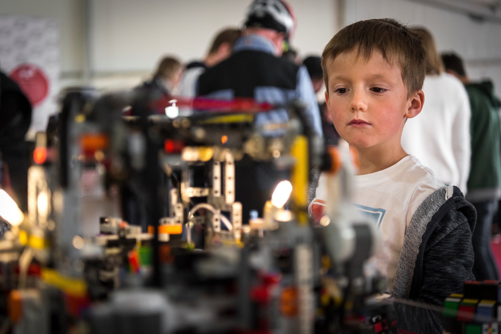 Un enfant captivé par un robot Lego capable de résoudre un rubik's cube.