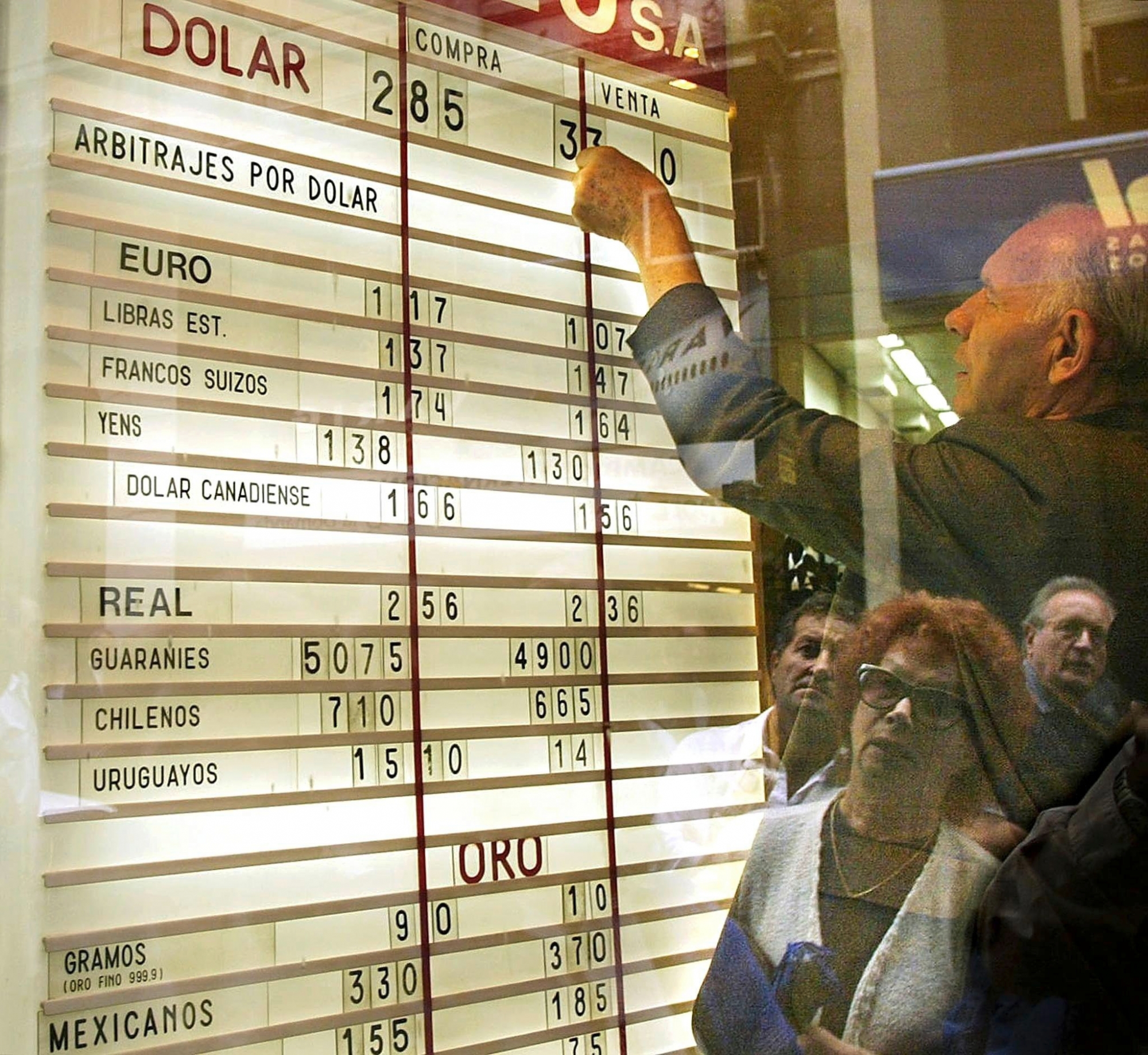 An employee of a currency exchange house places the dollar quotation in the shop window at market opening 25 March 2002 as people look on.  Crisis-hit Argentina said Friday it expected an IMF mission to visit Buenos Aires in early April to develop a support package.   (KEYSTONE/EPA/AFPI DANIEL GARCIA)  ARGENTINA ECONOMY DOLLAR