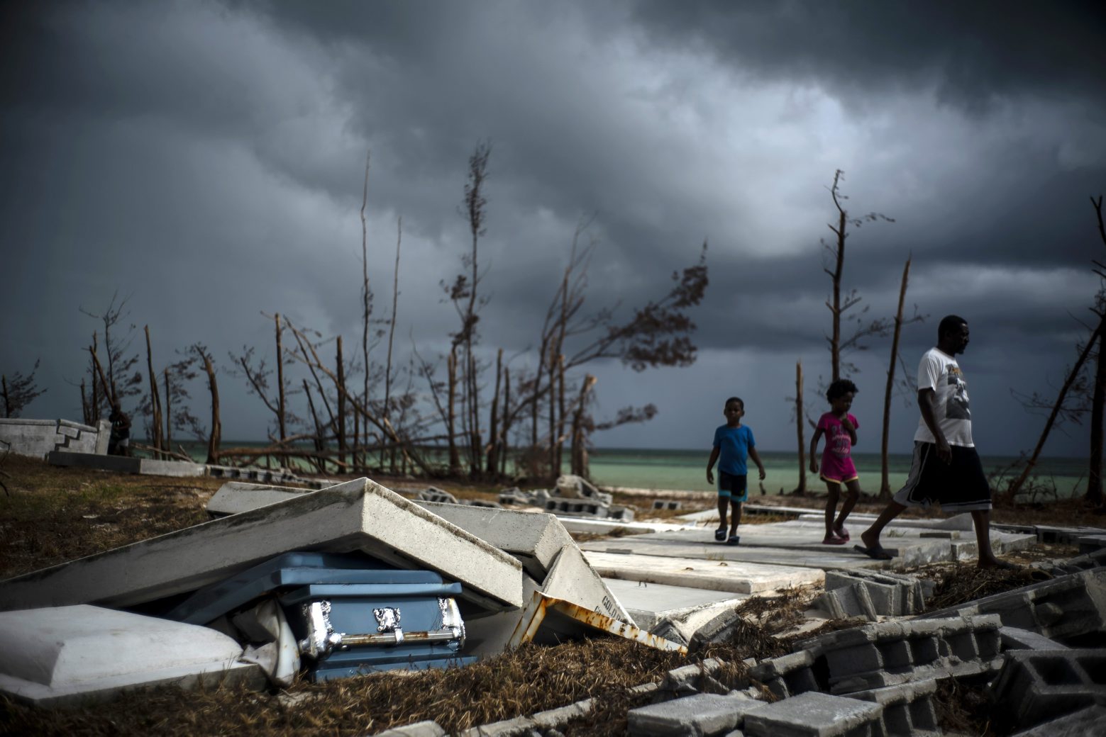 People walk next to a shattered and water-filled coffin lays exposed to the elements in the aftermath of Hurricane Dorian, at the cemetery in Mclean's Town, Grand Bahama, Bahamas, Friday Sept. 13, 2019. (AP Photo/Ramon Espinosa) Bahamas Hurricane Dorian