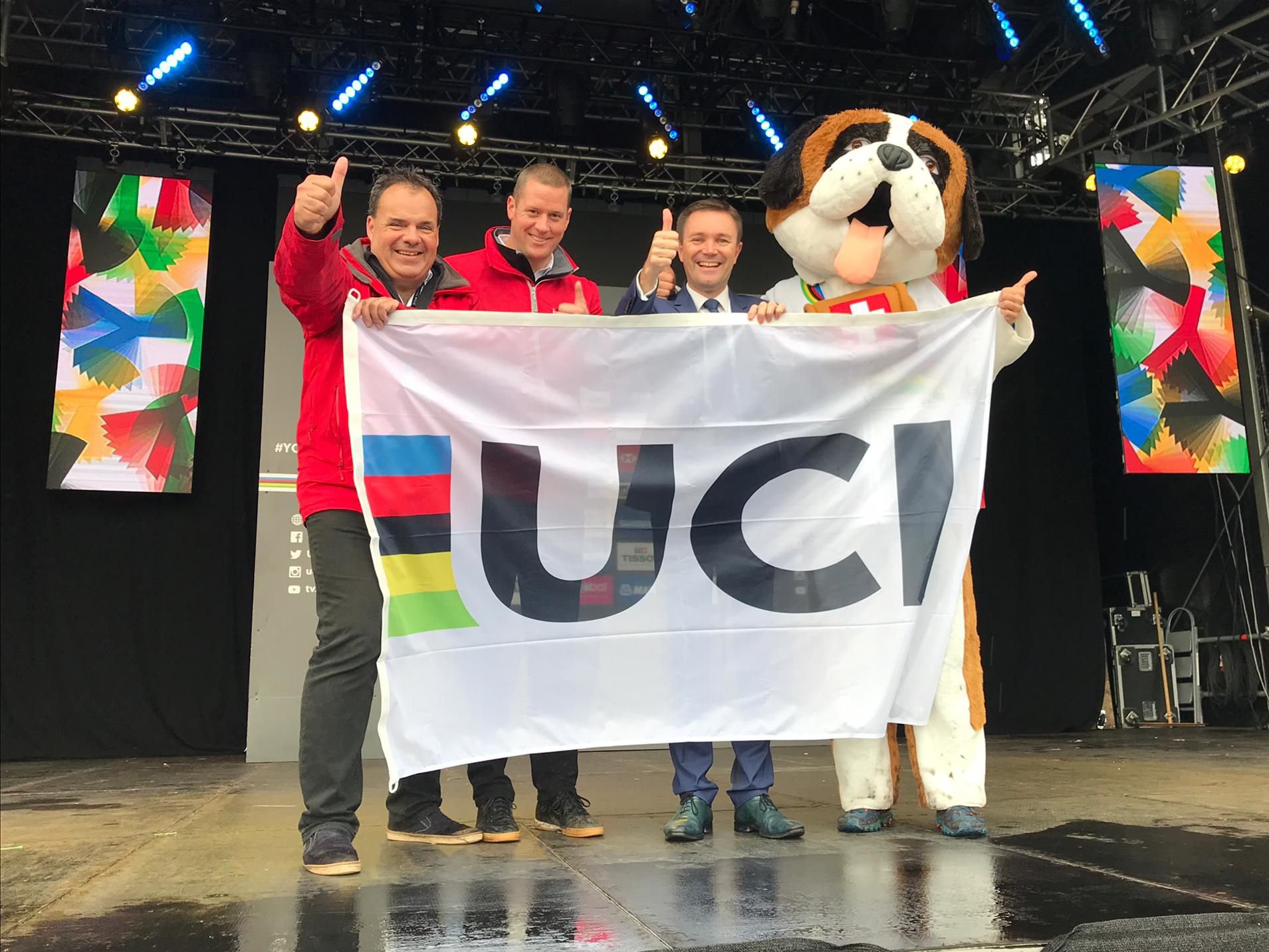 David Lappartient (troisième depuis la gauche) a remis le drapeau de l'UCI à Alexandre Debons et Grégory Devaud, les deux présidents du comité d'organisation, sous le regard de la mascotte, Barry.