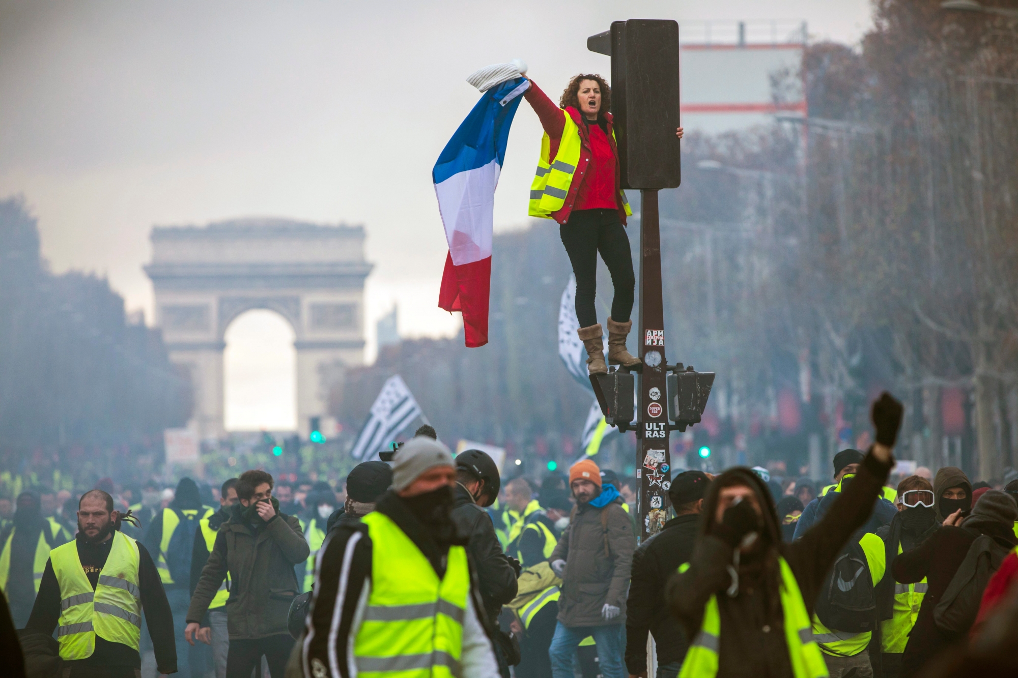 epa07186248 A woman wearing a yellow vest, as a symbol of French driver's and citizen's protest against higher fuel prices, waves a French flag during clashes with police forces on the Champs Elysee as part of a nationwide protest in Paris, France, 24 November 2018. The so-called 'gilets jaunes' (yellow vests) protest movement, which has reportedly no political affiliation, is protesting over fuel prices.  EPA/CHRISTOPHE PETIT TESSON FRANCE FUEL TAXES PROTEST