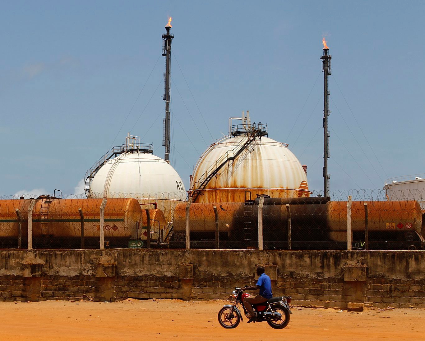 epa05281730 A photograph made available 28 April 2016 shows a motorcyclist riding in front of the Ivorien Society of Refinage facility (Société Ivoirienne de Refinage (SIR) in Abidjan, Ivory Coast 26 April 2016. According to global energy consultancy group Wood Mackenzie Africa's place as a significant producer and net exporter of oil in the world is forecast to grow to 15 per cent by 2020 due to new discoveries in West Africa. Substantial growth potential exists in West Africa with 40 billion barrels of discovered but undeveloped reserves and 55 billion barrels of yet-to-find oil. Since Jubilee discovery in 2007 companies are exploring other parts of the region between Ghana to Mauritania looking for analogous Cretaceous turbidite prospects. Offshore explorations in Sierra Leone and the Ivory Coast are high potential areas for investment beyond that of Nigeria and Angola.  EPA/LEGNAN KOULA ELFENBEINKUESTE BENZIN
