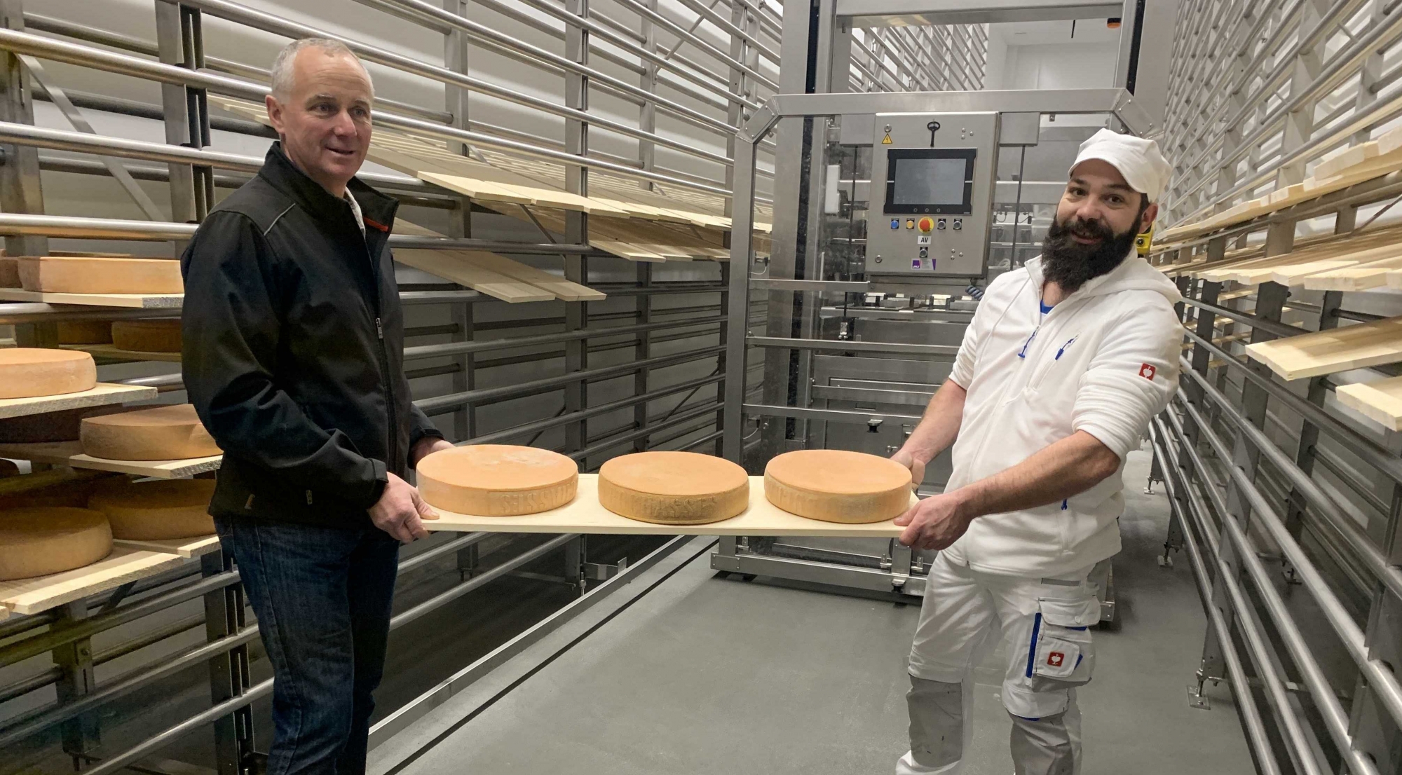 Le président de la Promovi, Laurent Ecoeur et le fromager responsable Gregory Gex-Fabry prennent symboliquement possession des premiers fromages dans la nouvelle cave d'affinage de La Cavagne. Devant le robot qui prendra le relais dès demain.