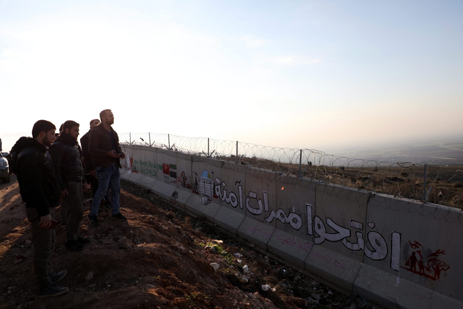 epaselect epa08188241 Syrian people look on as they stand at the Syrian-Turkish border wall with Arabic reading 'open safe passages' during a protest northwestern of Idlib, Syria, 02 February 2020. According to local reports, some 500 people joined the protest titled 'From Idlib to Berlin' organized by several civilian activists in northern Syria to highlight the sufferings of Idlib residents after the Syrian regime launched operation and escalated airstrikes on the area. According to one of the organizers, the protesting people are calling on Turkey to open safe passages so that civilians can cross to European countries, namely Germany which had previously received Syrian refugees.  EPA/YAHYA NEMAH epaselect SYRIA IDLIB PROTEST