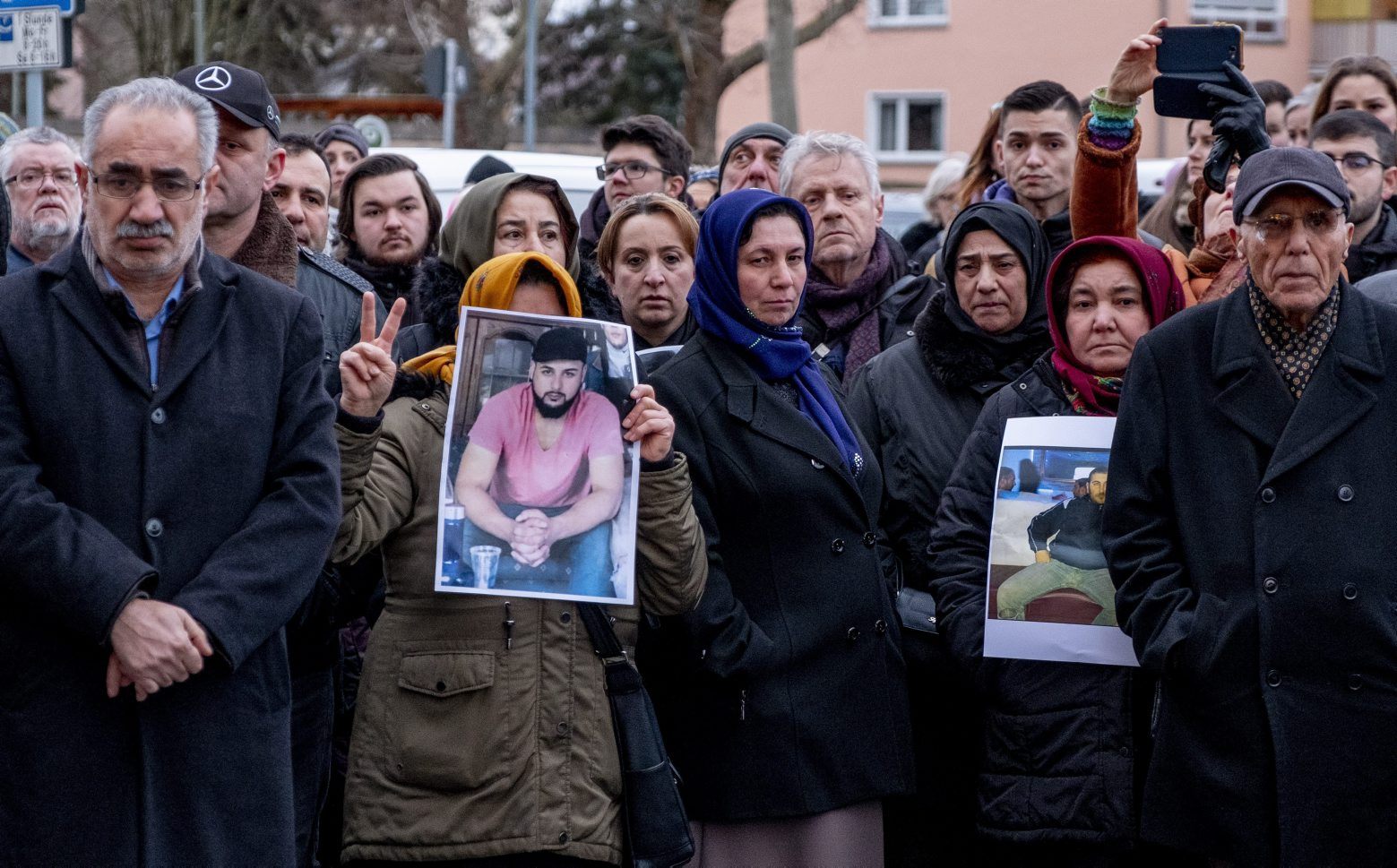 People hold photos of their friends, victims of a shooting in Hanau, Germany, on Friday, Feb. 21, 2020. A 43-year-old German man shot dead nine people of immigrant backgrounds in the Frankfurt suburb of Hanau on Wednesday night before killing his mother and himself. He left a number of rambling texts and videos espousing racist views. (AP Photo/Michael Probst) Germany Shooting
