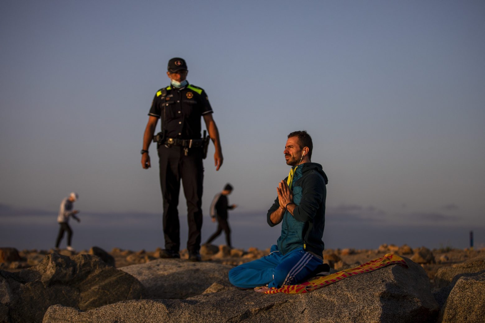 A police officer talks to a man meditating in a beach reopened for sport activities after the lockdown measures imposed by the government in Barcelona, Spain, Friday, May 8, 2020. In last minute negotiations, Spain's government has secured enough parliamentary support to extend later on Wednesday the country's state of emergency. Spain has recorded over 25,600 deaths from the new coronavirus. (AP Photo/Emilio Morenatti) APTOPIX Virus Outbreak Spain